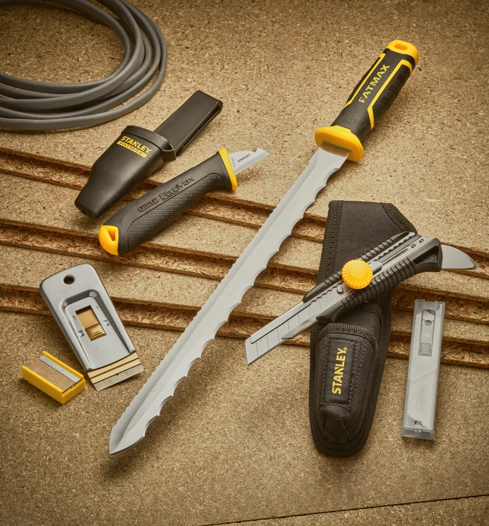 STANLEY 0-28-500 Set mit Handwerkzeugen, Schneidemessern, Raspel, Ersatzklingen und schwarz-gelben Griffen auf beigem Untergrund.
