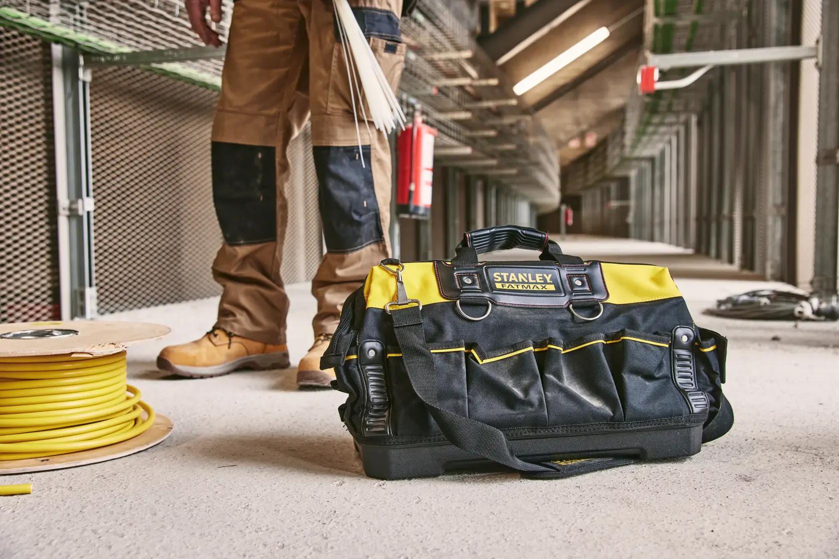 STANLEY 1-93-950 Werkzeugtasche in Schwarz und Gelb mit Griffen, auf einer Baustelle neben Kabelrolle.