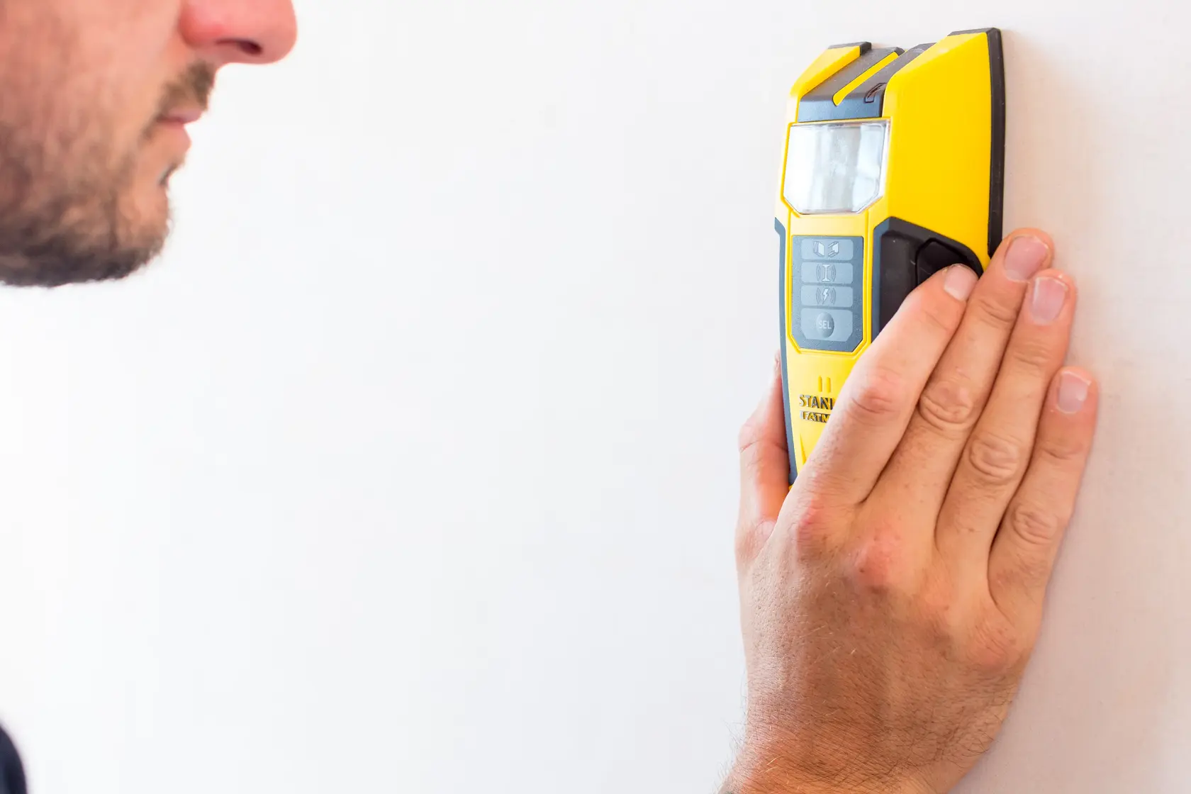 STANLEY FMHT0-77407 gelber Leitungsfinder von einer Hand an einer weißen Wand gehalten, Frontansicht.