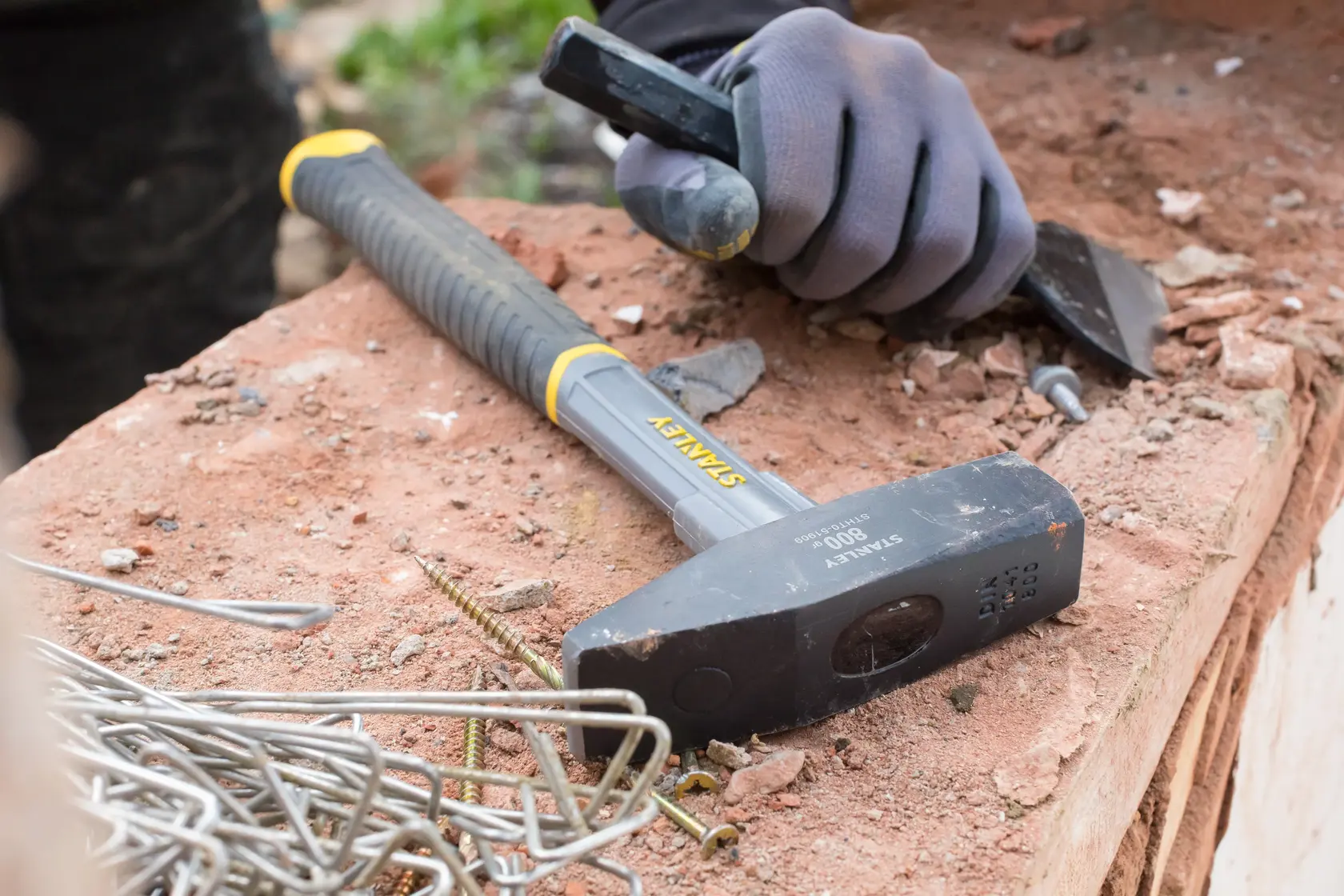 STANLEY STHT0-51909 Vorschlaghammer mit schwarzem Griff auf Werkbank neben Metallbefestigungen und behandschuhter Hand.