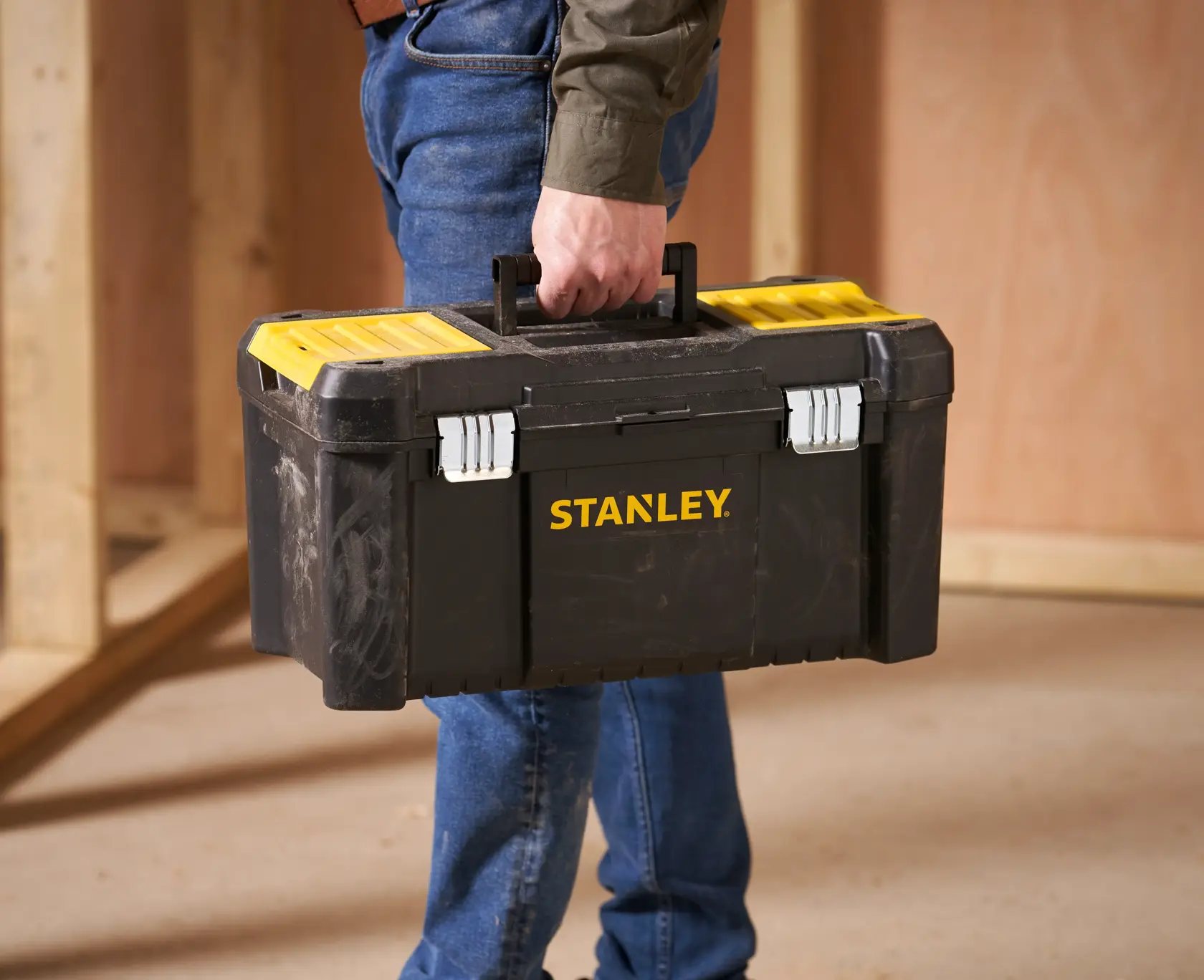 Stanley STST1-75521 schwarze und gelbe Werkzeugbox, von einer Person getragen, in Werkstattumgebung.