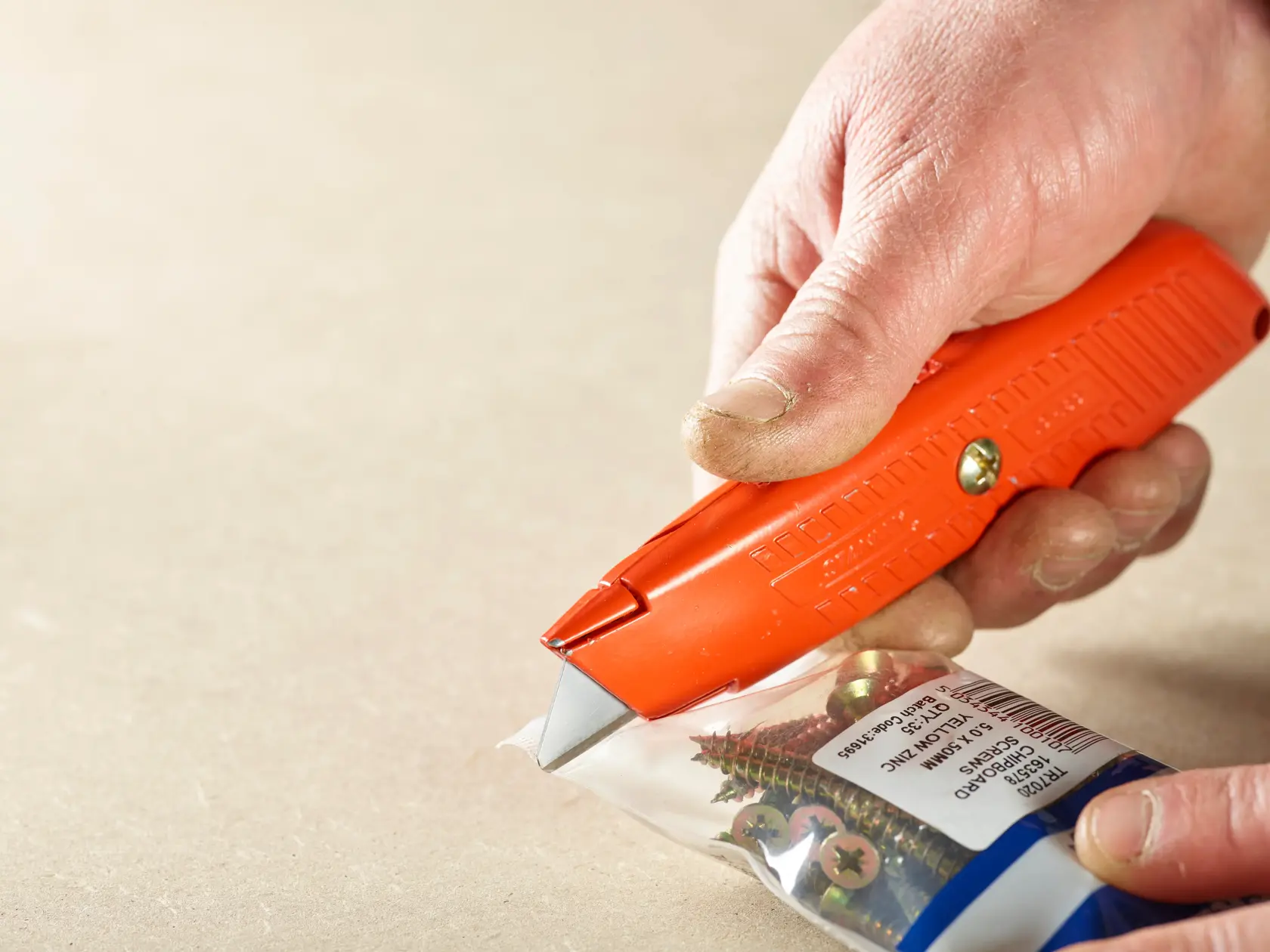 STANLEY 0-10-189 orange Universalmesser schneidet Plastiktüte mit Schrauben, Nahaufnahme Fotografie.