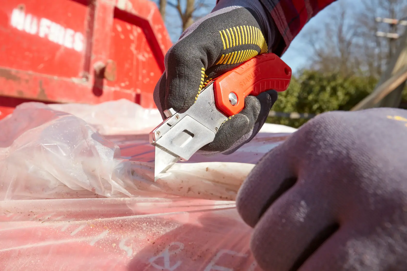 Foto vom STANLEY 0-10-243 Universalmesser beim Schneiden von Plastikfolie im Freien, Arbeiter mit Handschuhen.