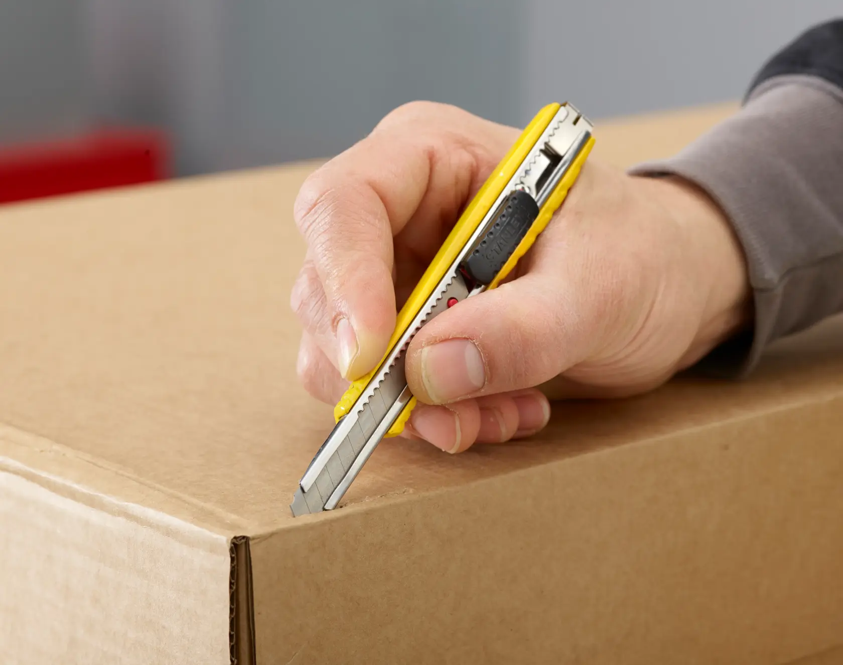 STANLEY 0-10-411 yellow utility knife cutting cardboard box, close-up in use.