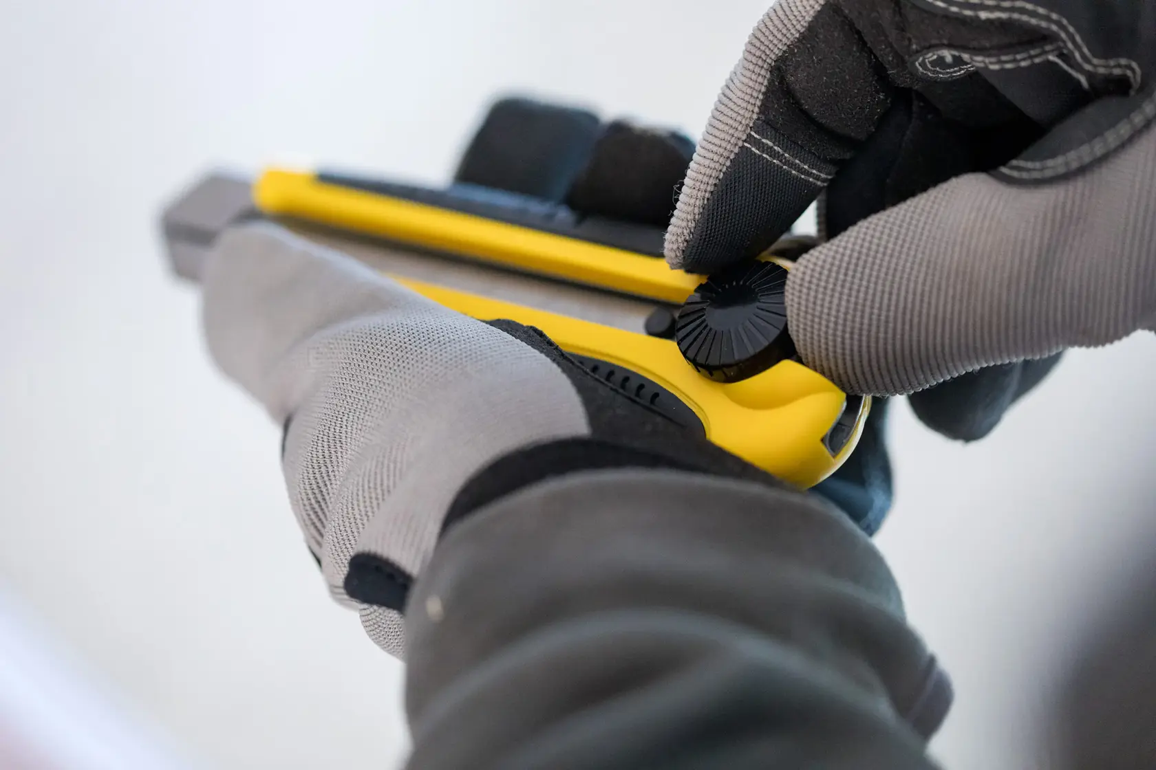 Photo of STANLEY 0-10-425 utility knife held in gloved hands, close-up showing adjustment knob.