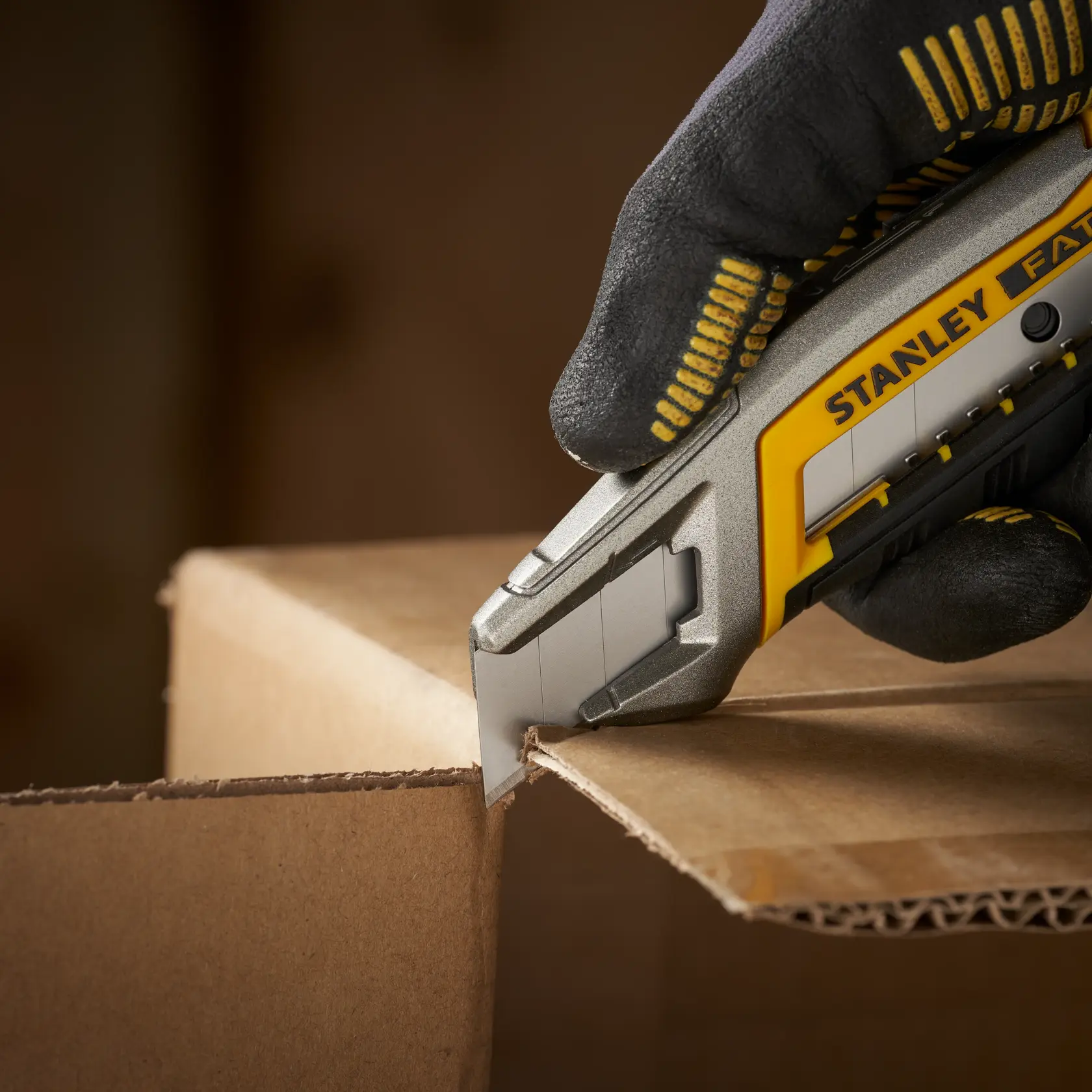 Foto des STANLEY 0-11-301 Cuttermessers, das Karton schneidet, Nahaufnahme mit behandschuhter Hand.