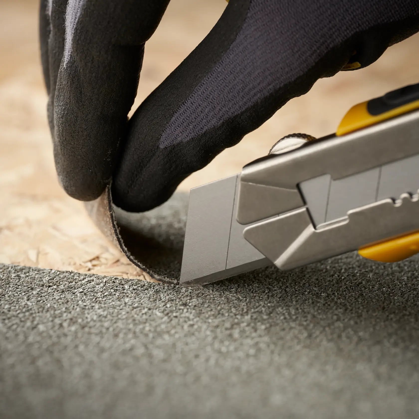 STANLEY 0-11-725 utility knife cutting roofing material, close-up, with gloved hand holding material.