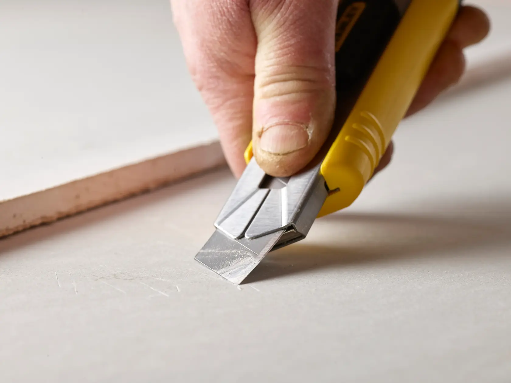 Photo of STANLEY 0-11-725 utility knife cutting drywall, close-up of the blade and yellow handle.