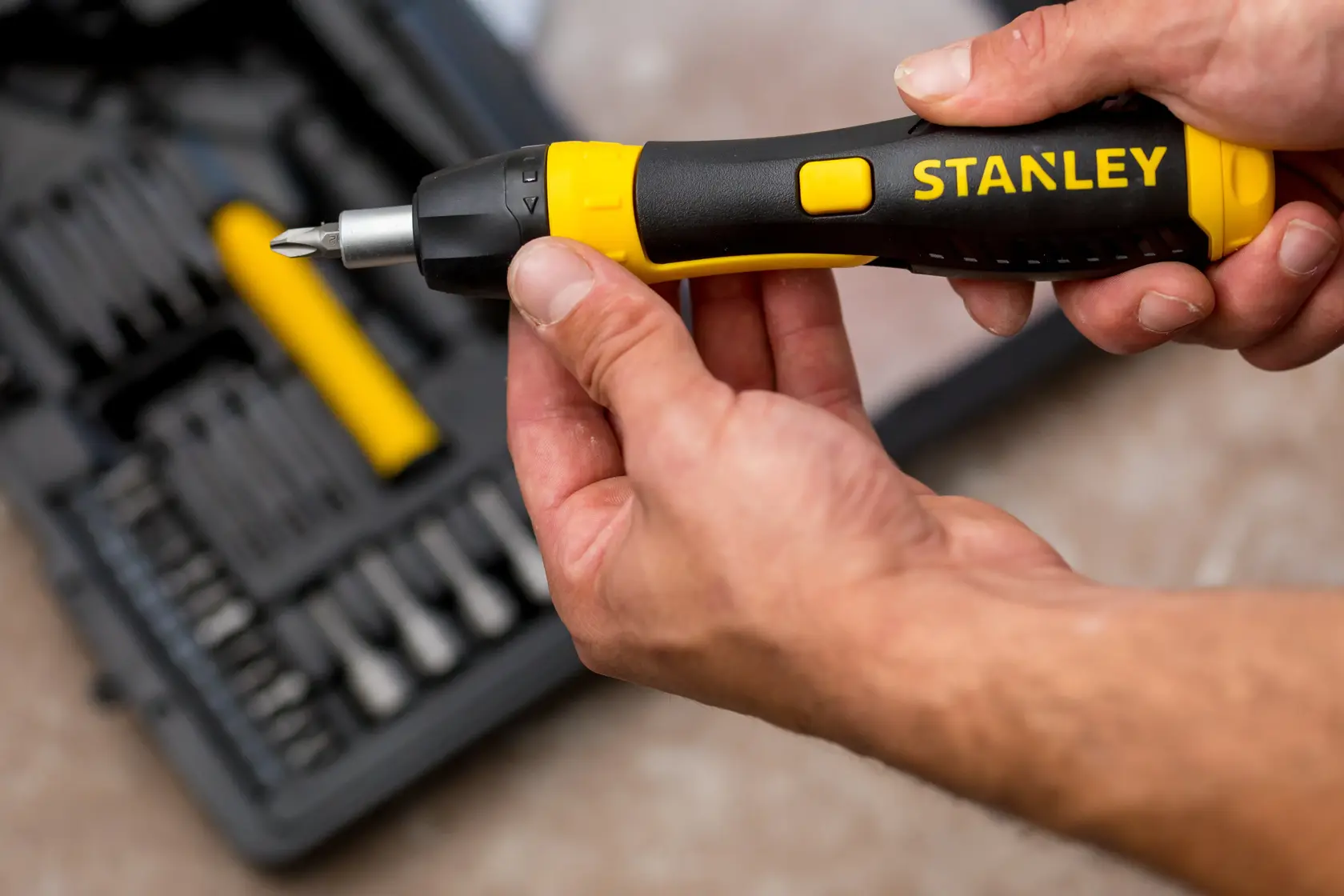 STANLEY 0-63-038 Ratschen-Schraubendreher mit schwarz-gelbem Griff in Hand, Werkzeugkasten im Hintergrund.
