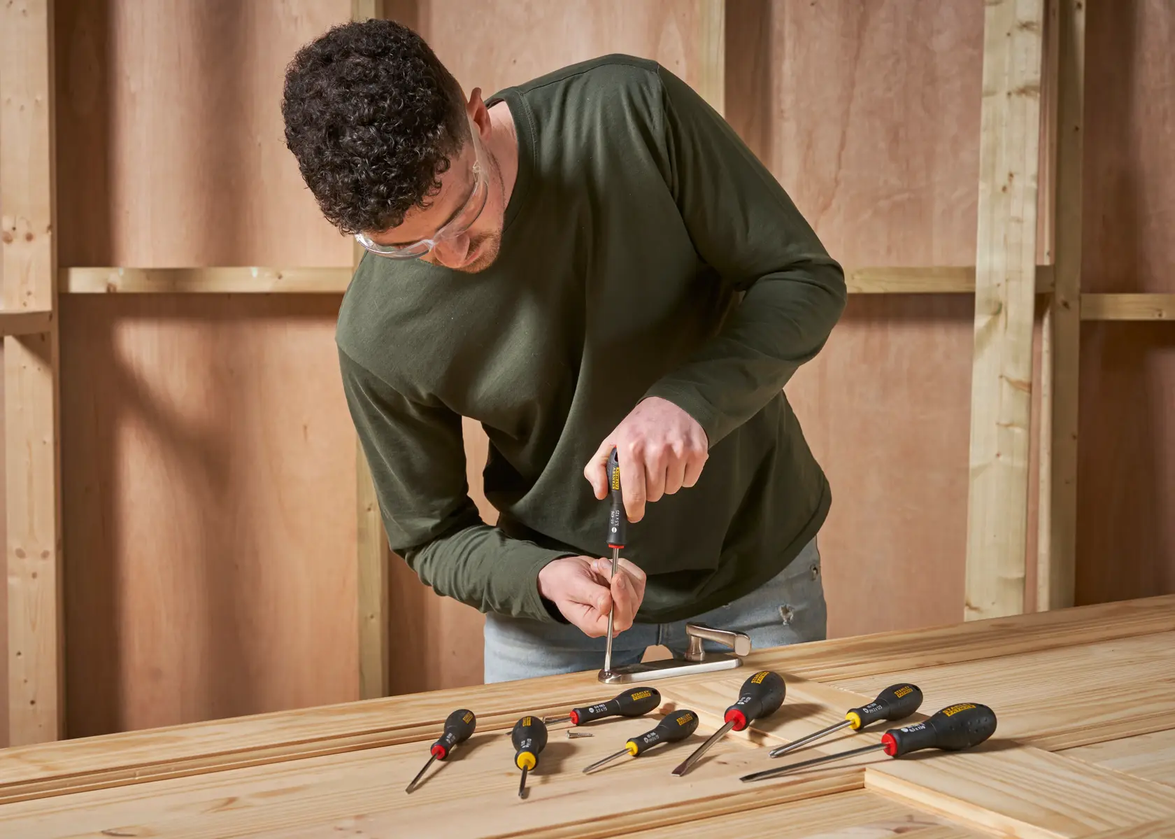 Photo of STANLEY 0-65-437 screwdrivers set on wooden table with worker using one in workshop.
