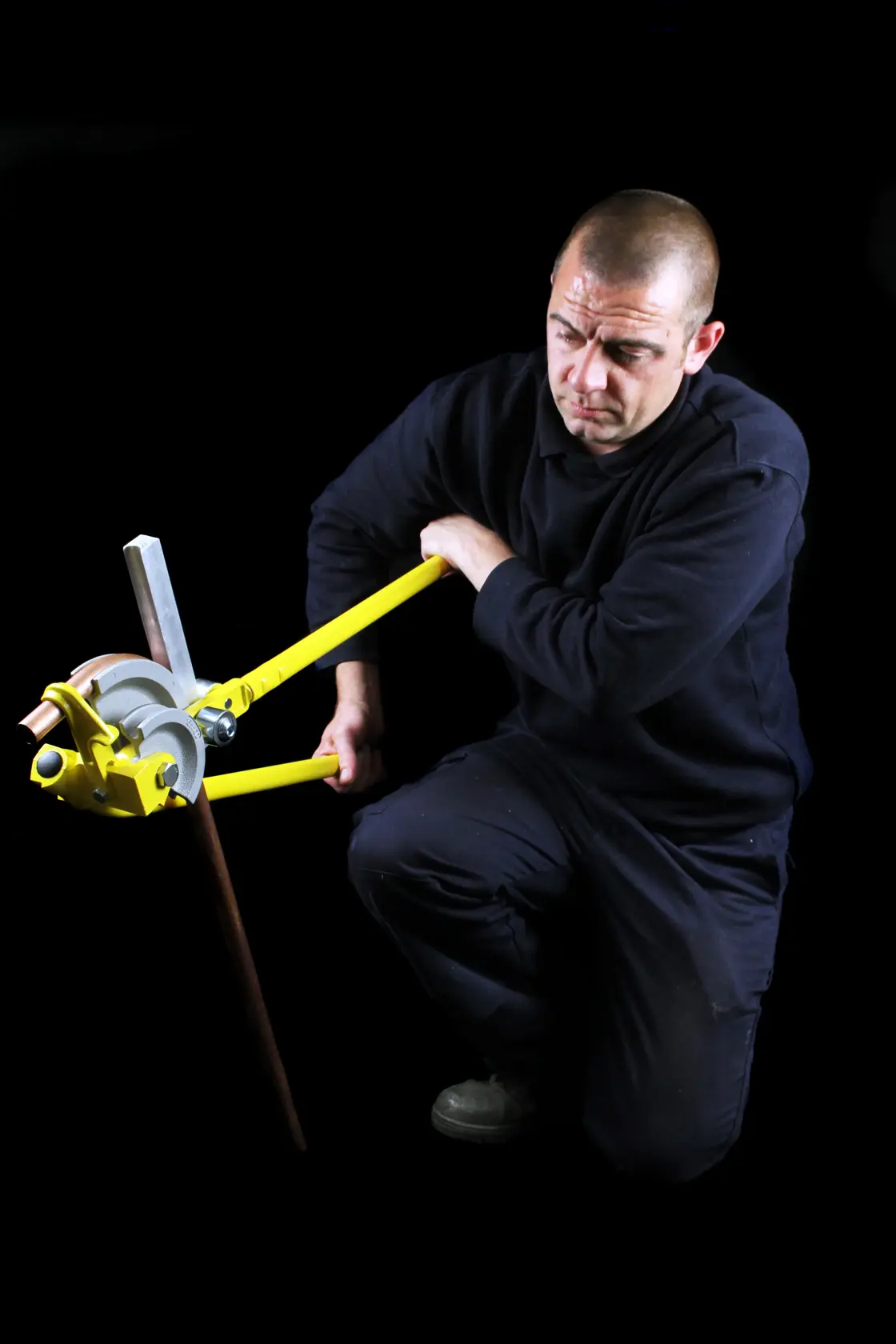Photo of a person using STANLEY 0-70-452 pipe bender tool on a metal pipe, against a black background.