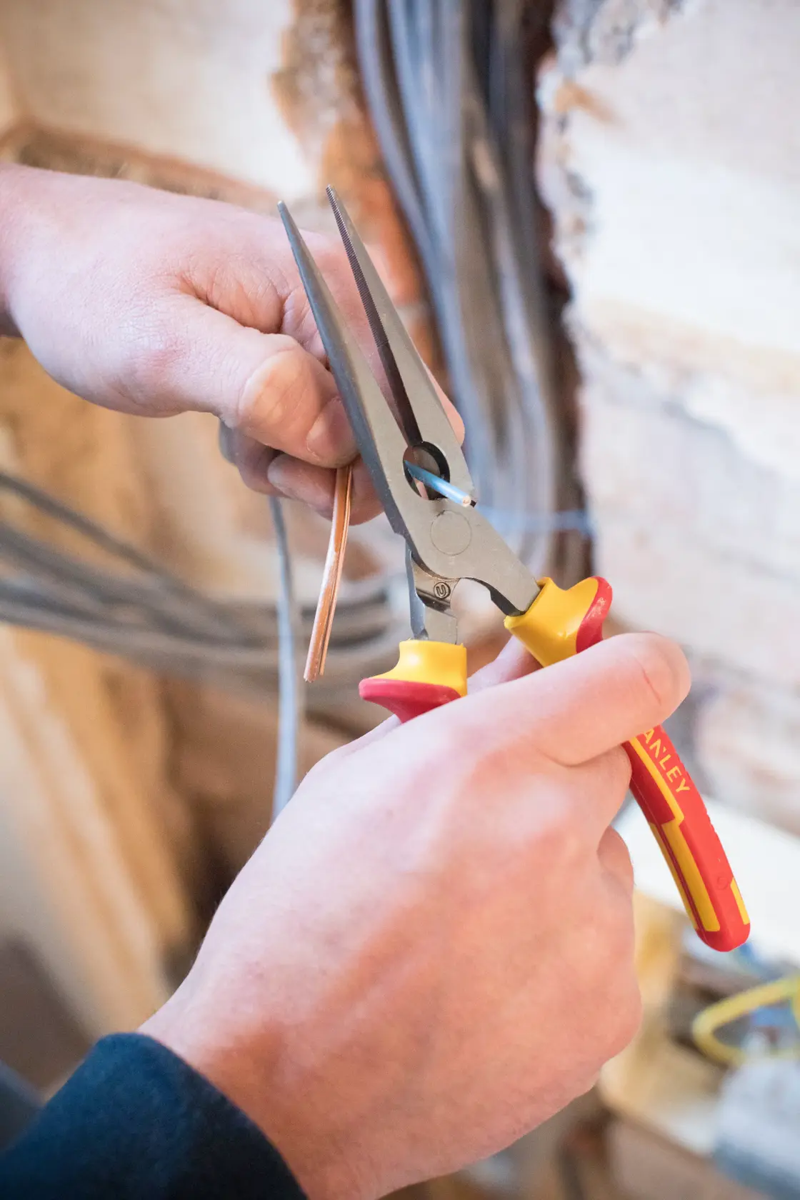 Photo of STANLEY 0-84-007 long nose pliers with red and yellow handles gripping copper wire, close-up in use.