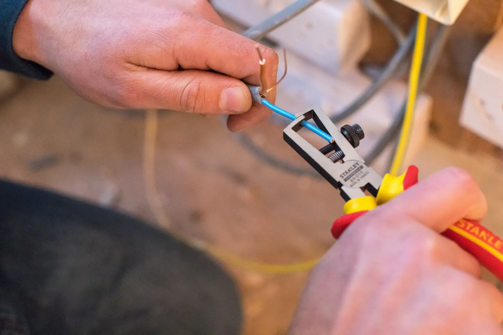 STANLEY 0-84-010 Abisolierzange im Einsatz, entfernt Isolierung von blauem Elektrokabel bei der Installation.
