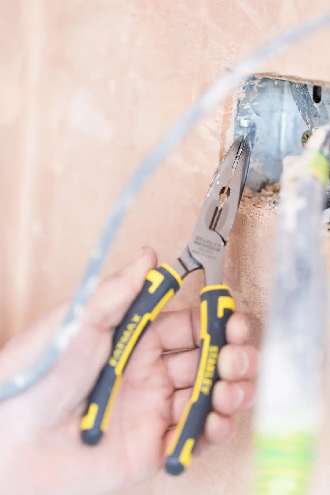 STANLEY 0-89-872 long nose pliers with black and yellow handles used for wiring in construction wall.