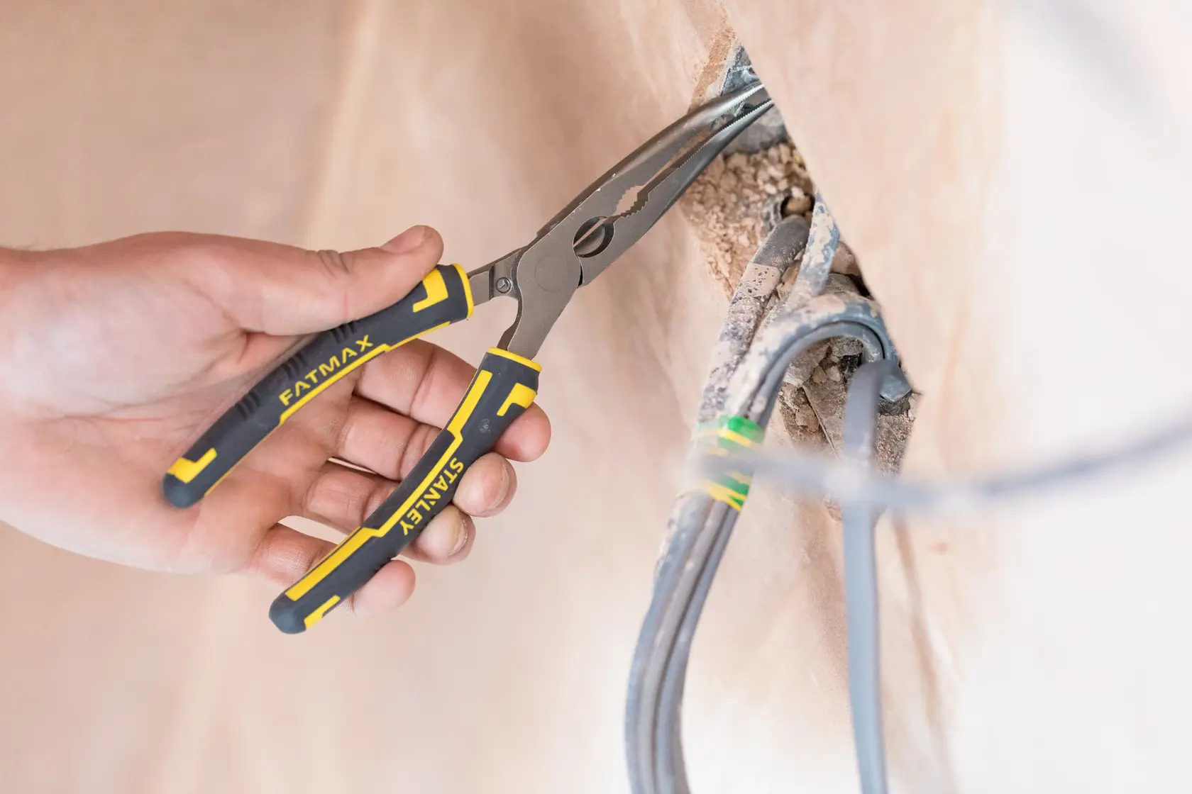 Stanley 0-89-872 FATMAX pliers used to grip electrical wires, black and yellow handles, close-up view.