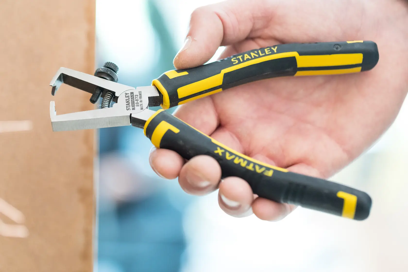 STANLEY 0-89-873 wire stripper pliers with black and yellow handle, held in hand, side view.