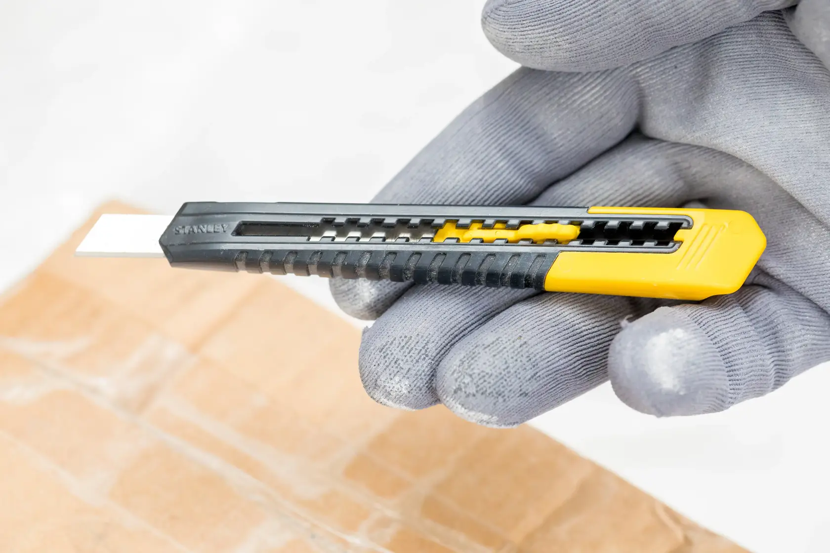 STANLEY 1-10-150 Universalmesser mit gelb-schwarzem Griff, gehalten in behandschuhter Hand, schneidet Karton.