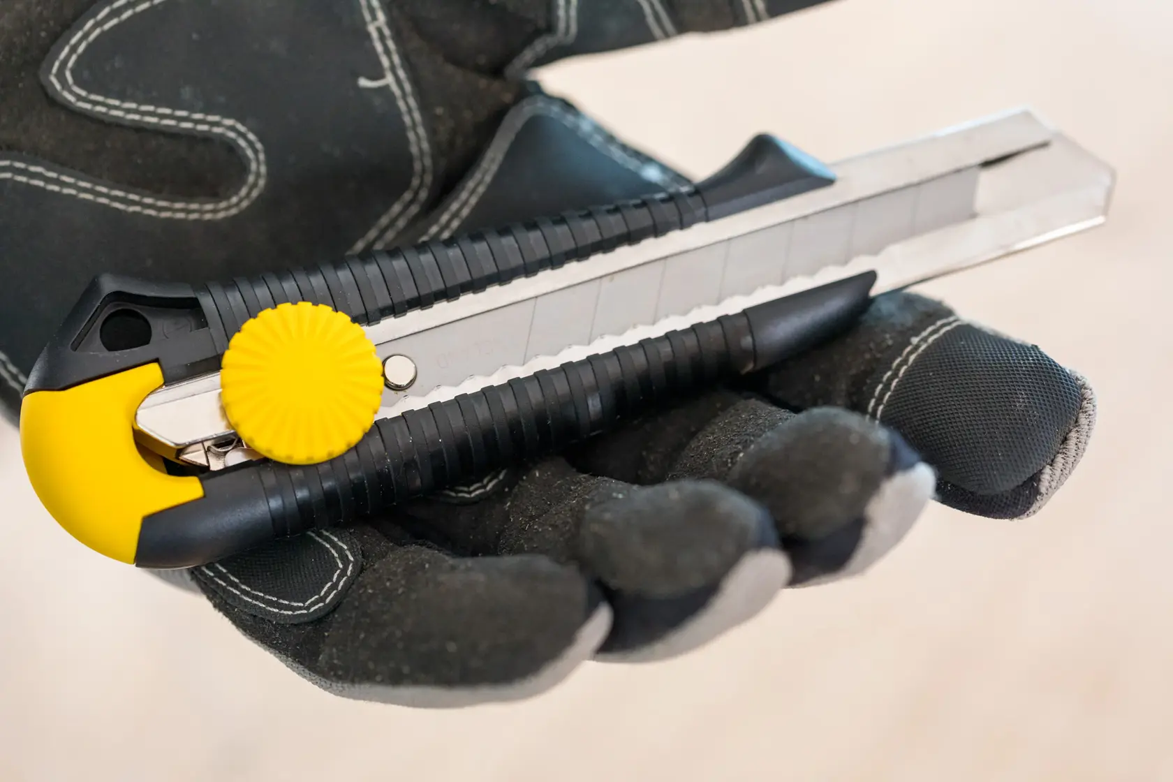 STANLEY 1-10-418 utility knife with yellow knob held in gloved hand, photography close-up angle.