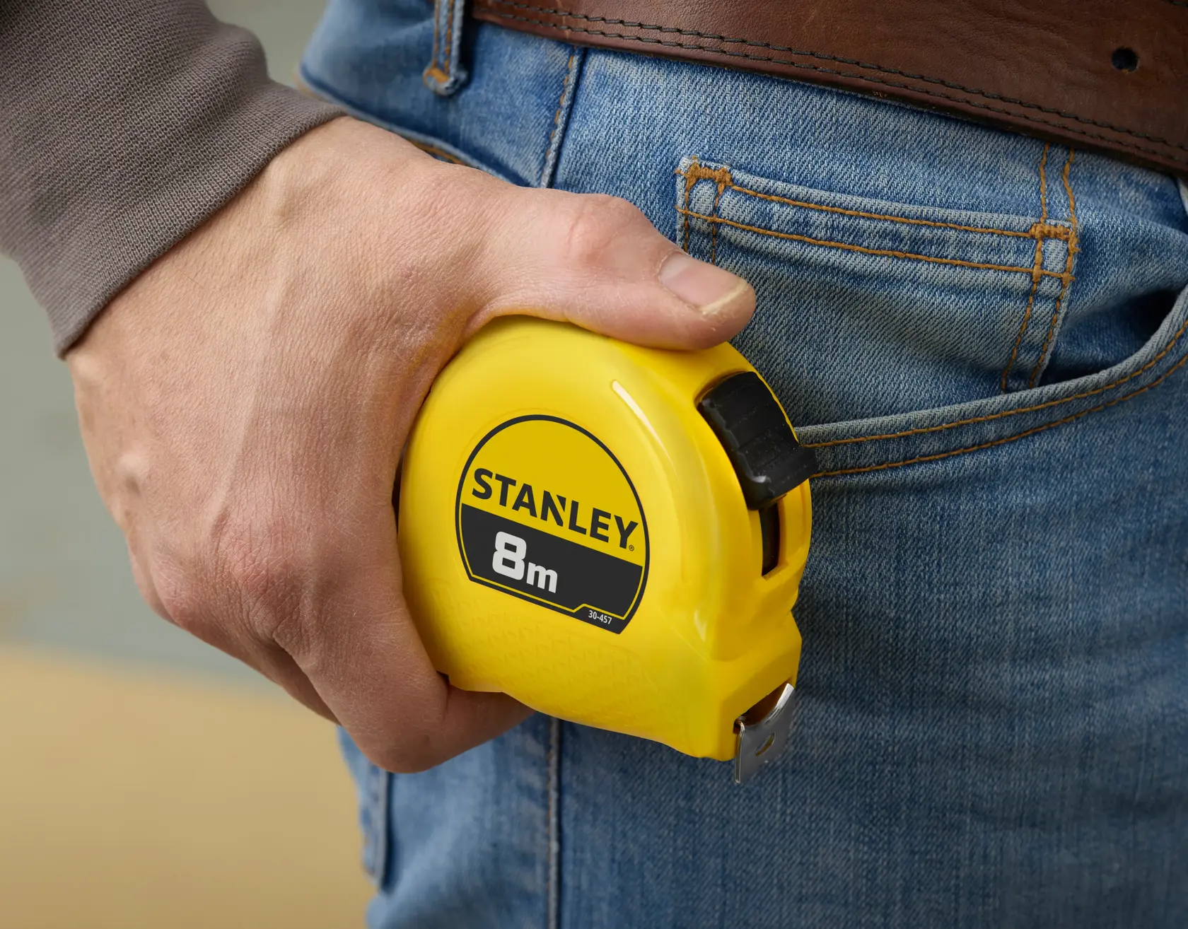 STANLEY 1-30-457 gelbes 8m Maßband wird in der Hand nahe Jeans-Tasche gehalten, Nahaufnahme.