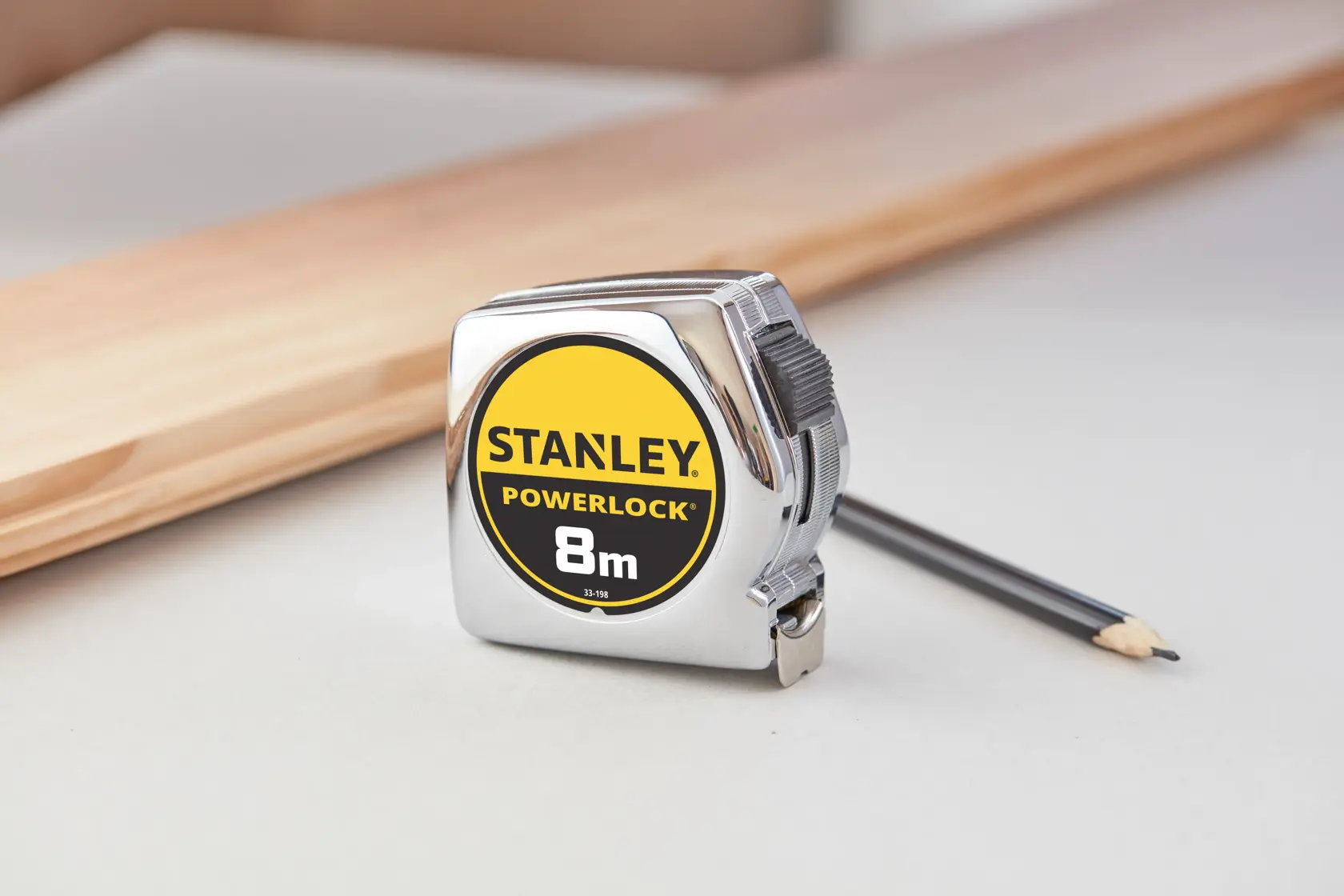 STANLEY 1-33-198 PowerLock 8m Bandmaß mit Chromgehäuse, auf Tisch neben Bleistift und Holz.