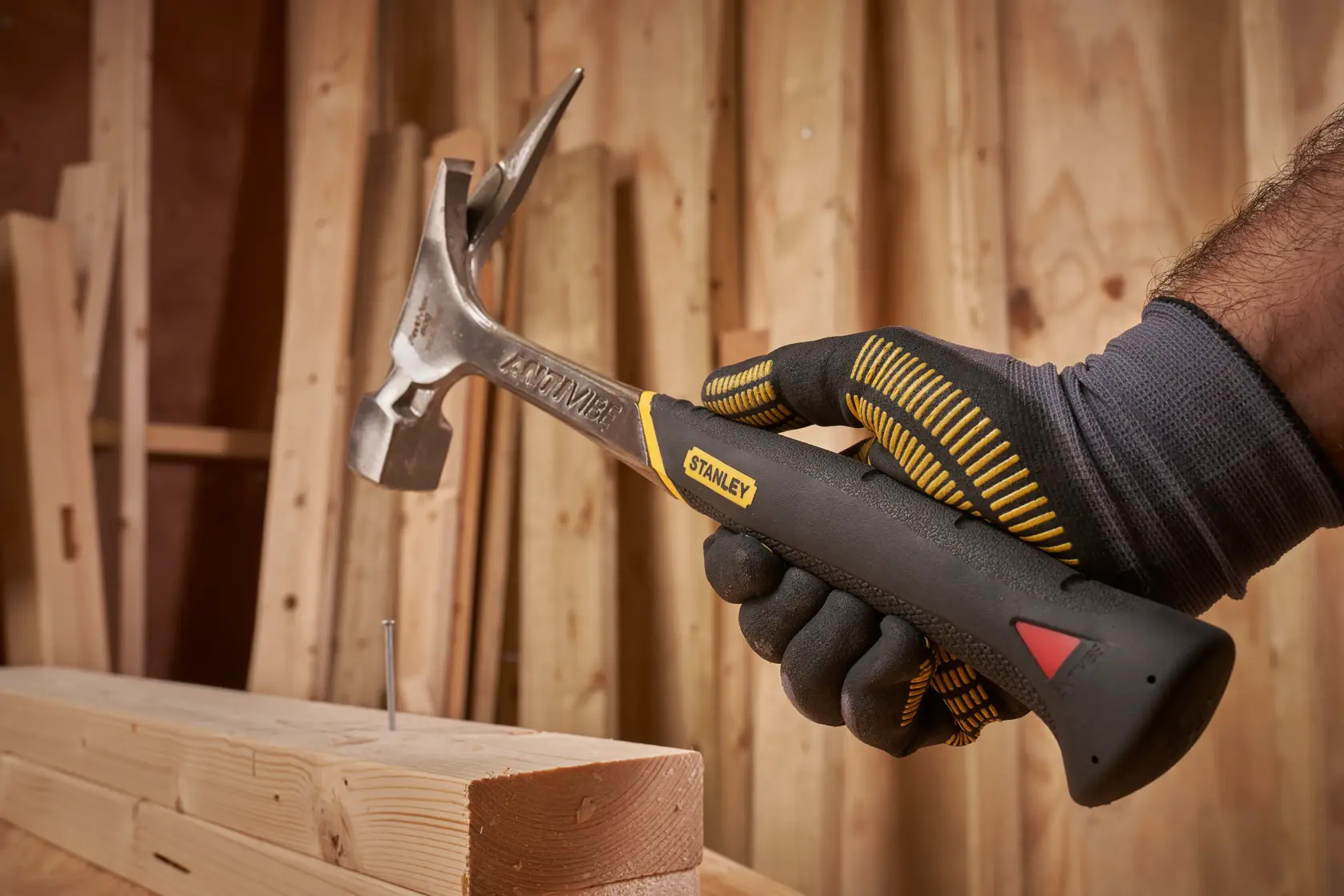 STANLEY 1-51-937 Klauenhammer in behandschuhter Hand, Nagel wird ins Holz geschlagen, Werkstatt Hintergrund.