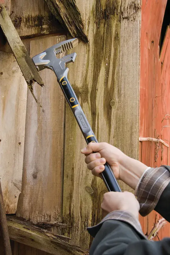 Stanley 1-55-120 demolition tool in use against wood, hand gripping black and yellow handle.