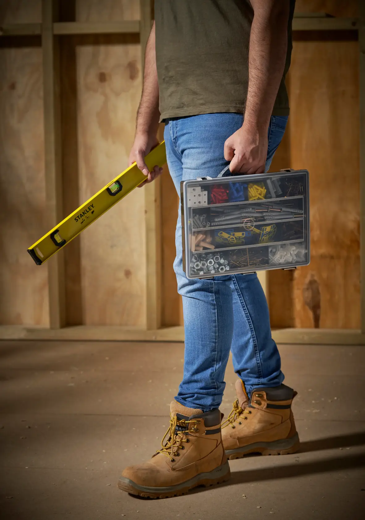 STANLEY 1-92-761 Hardware Organizer Koffer, getragen von Person mit hellen Arbeitsstiefeln auf Baustelle.