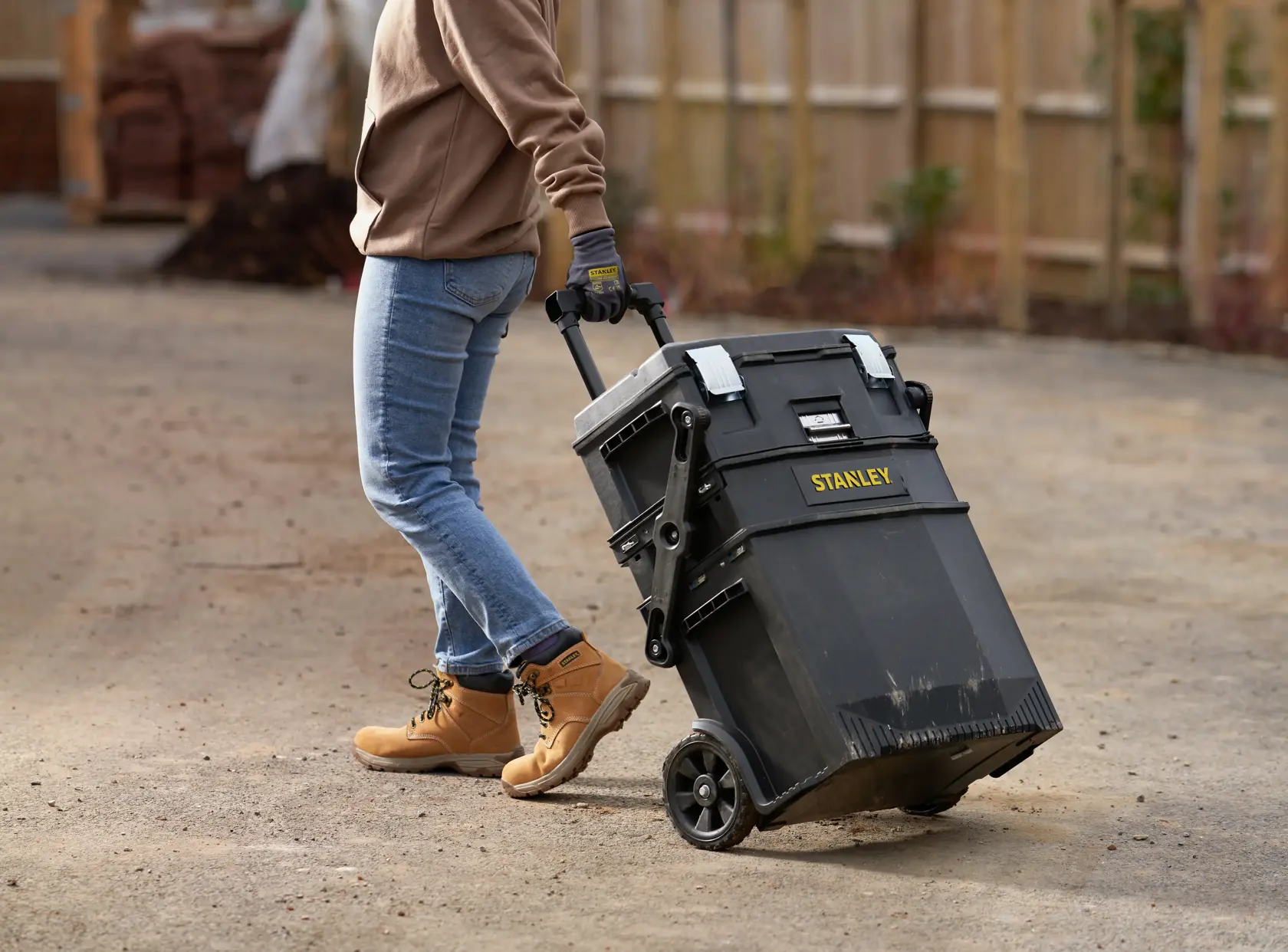 STANLEY 1-94-210 rollende Werkzeugbox wird im Freien von einer Person mit Jeans und Arbeitsstiefeln gezogen.
