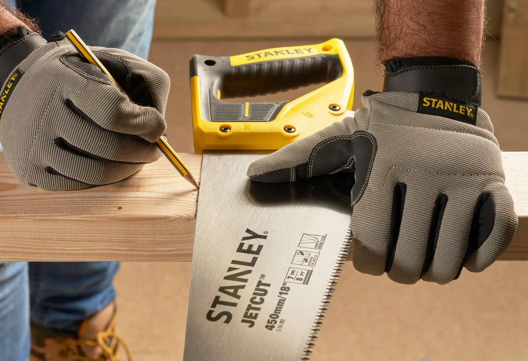 STANLEY 2-15-283 Handsäge mit gelbem Griff von behandschuhter Hand gehalten, Holzbrett wird markiert. Fotografie Vorderansicht.