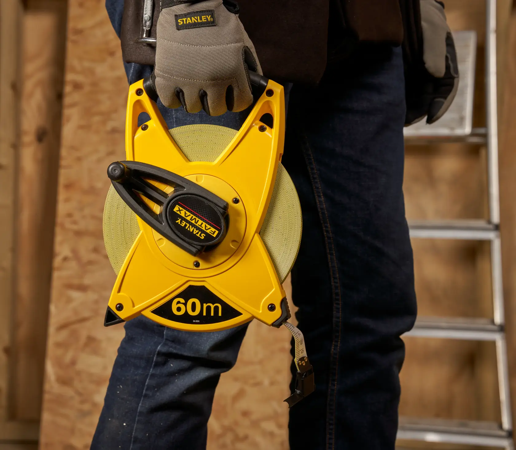 STANLEY 2-34-824 gelbes 60-m-Offenrollmaßband, gehalten von Arbeiter mit Handschuhen in Werkstatt.