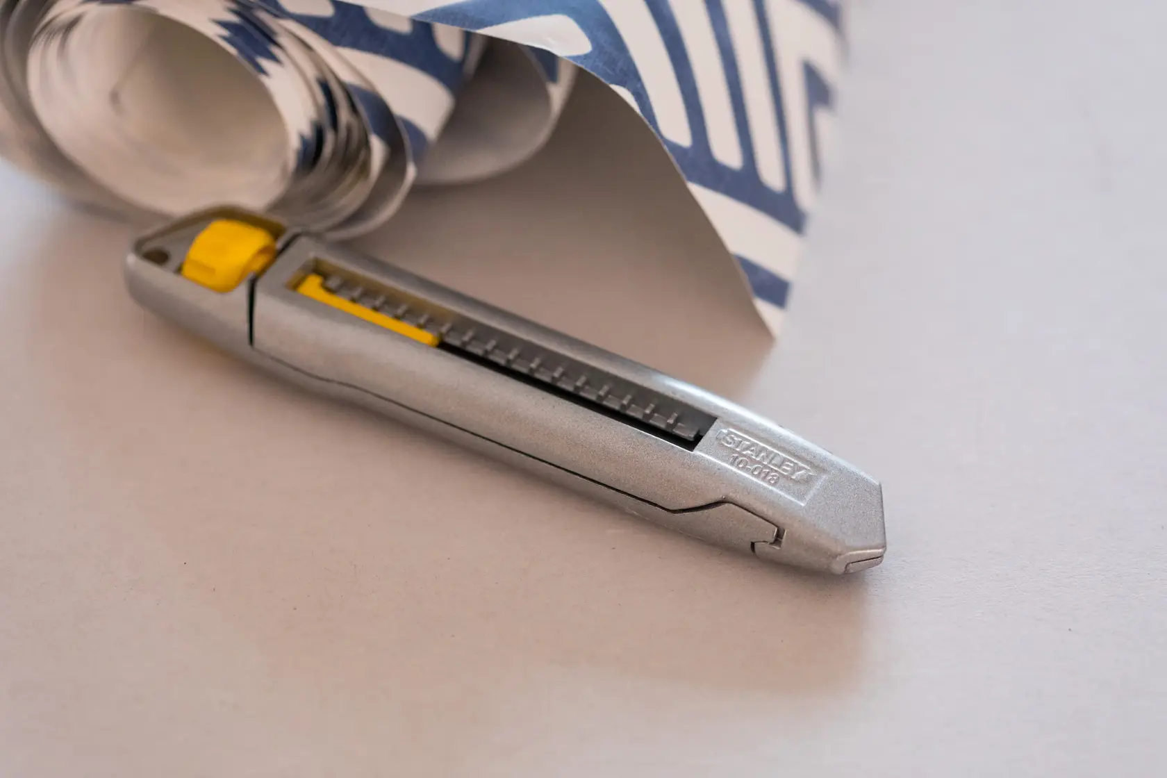 STANLEY 4-10-018 utility knife with silver body and yellow slider next to patterned rolled paper.