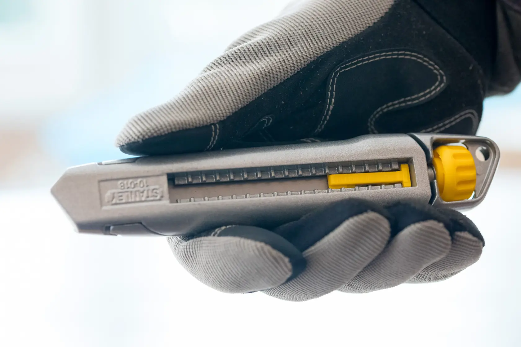 Photo of STANLEY 4-10-018 utility knife with gray body and yellow slider, held in a gloved hand.