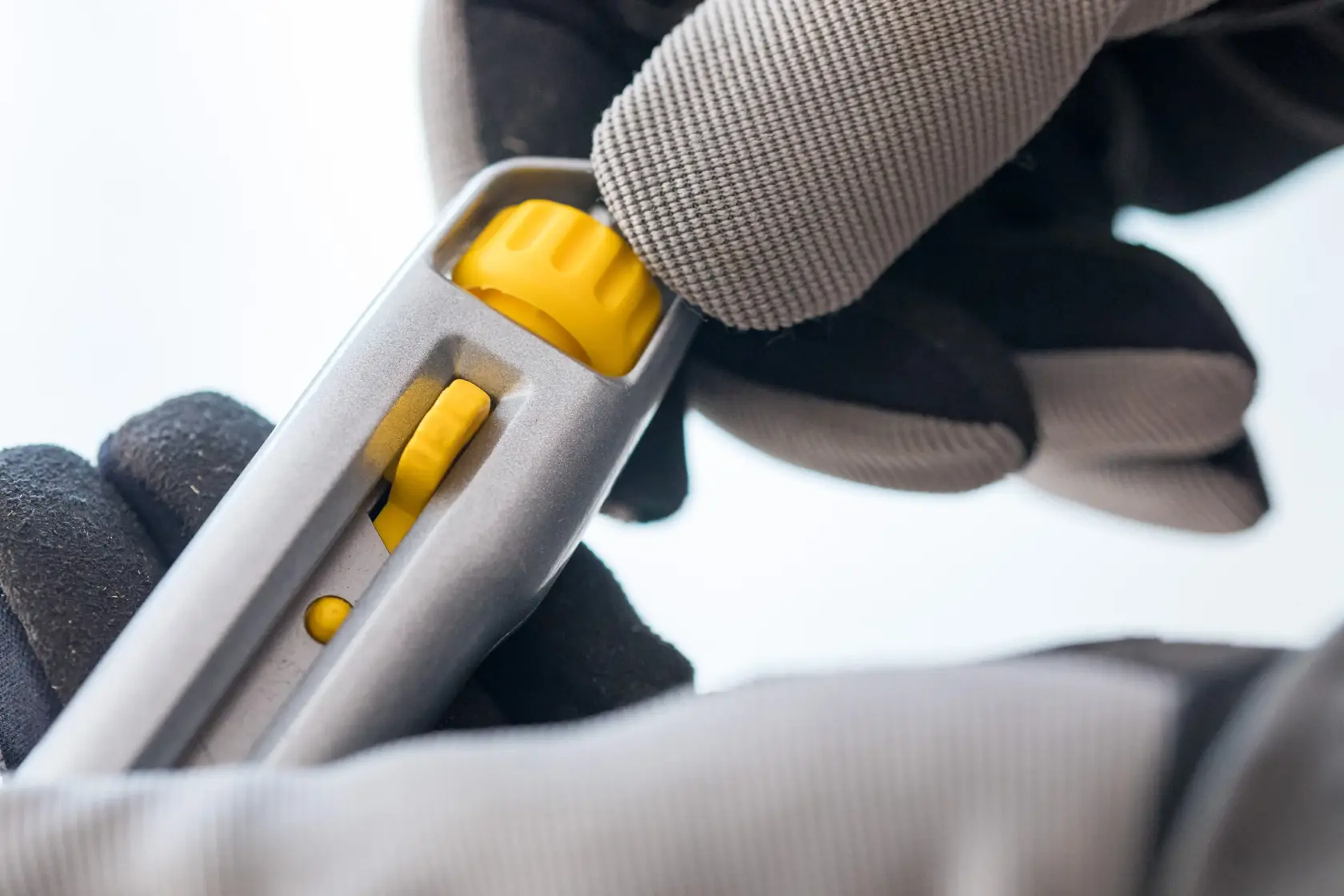 Photo of STANLEY 4-10-018 utility knife close-up showing yellow blade adjustment with gloved hand.