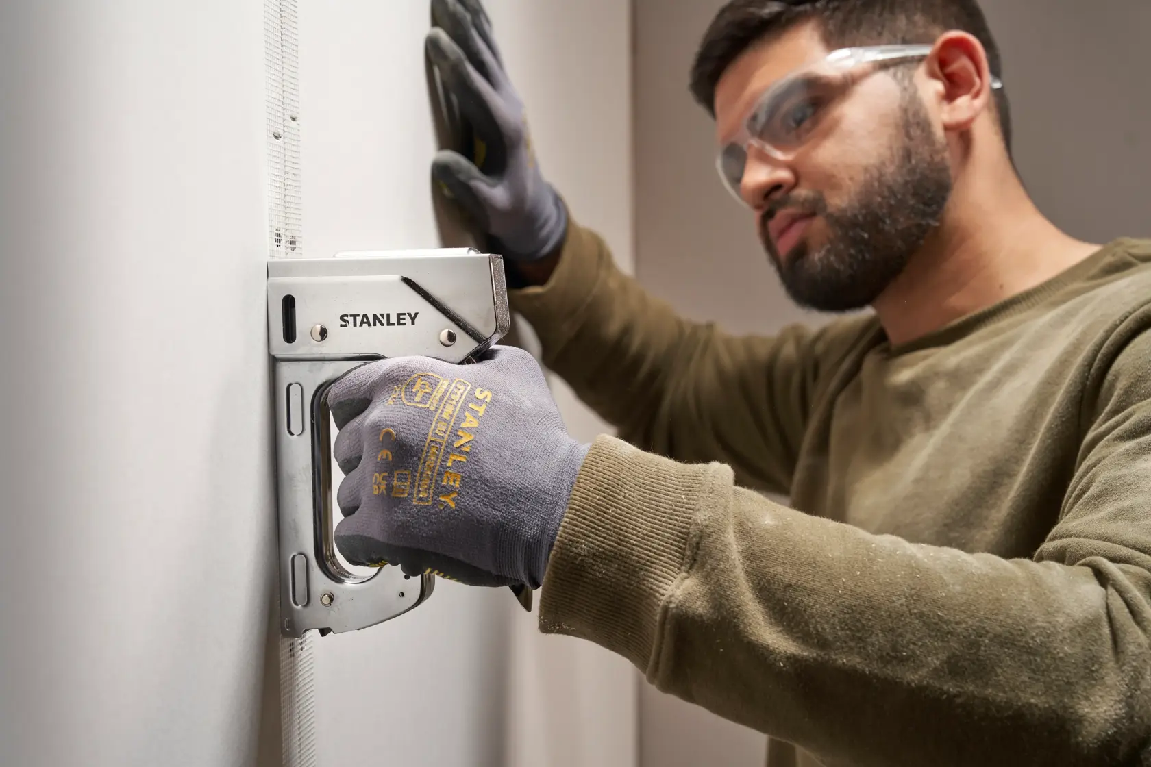 Foto des STANLEY 6-TR110 Tackers, verwendet an einer Wand von Person mit STANLEY Handschuhen.