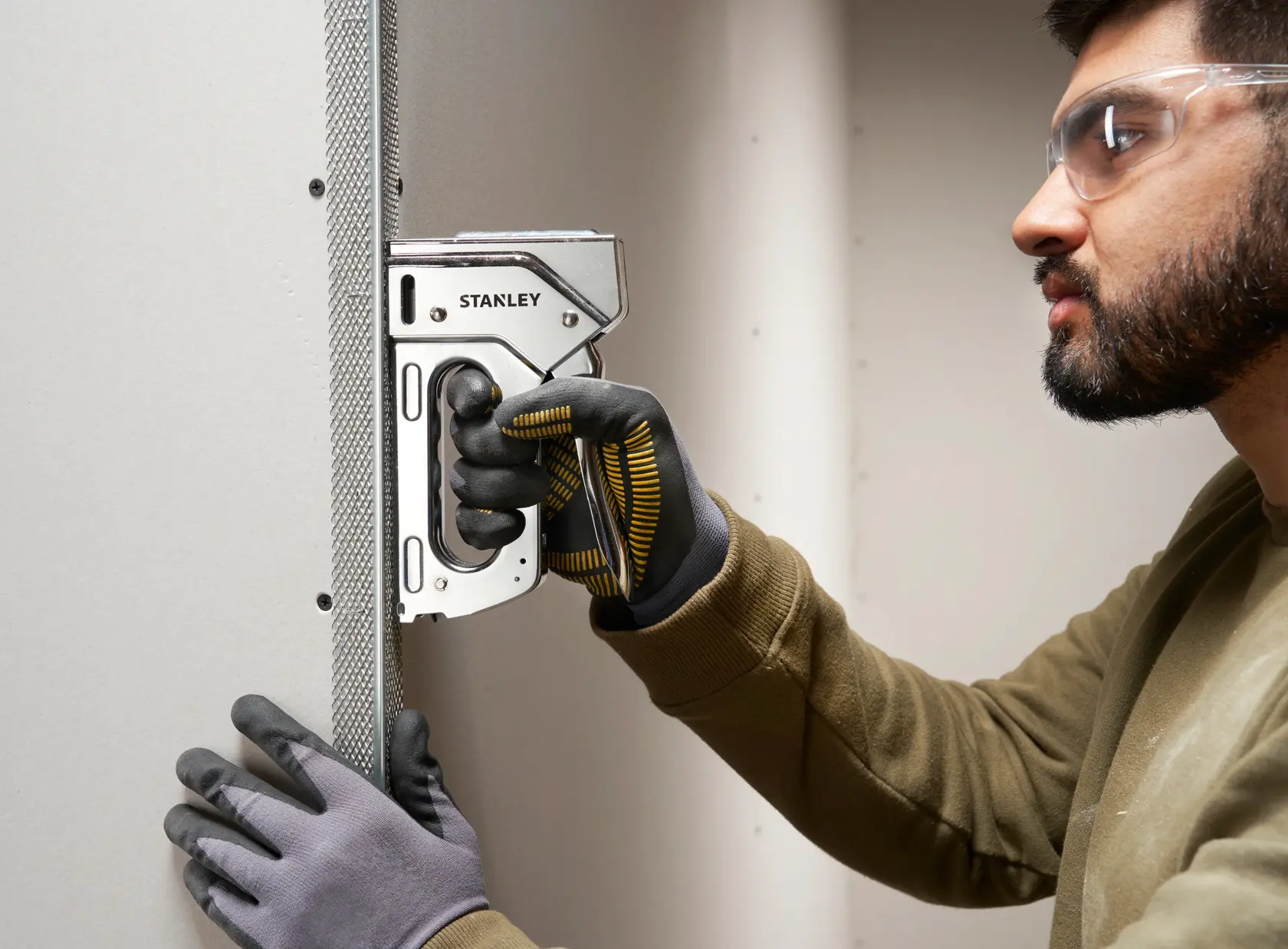 Stanley 6-TR110 Tacker für starke Beanspruchung, verwendet an Trockenbauwand, Nahaufnahme von behandschuhten Händen.