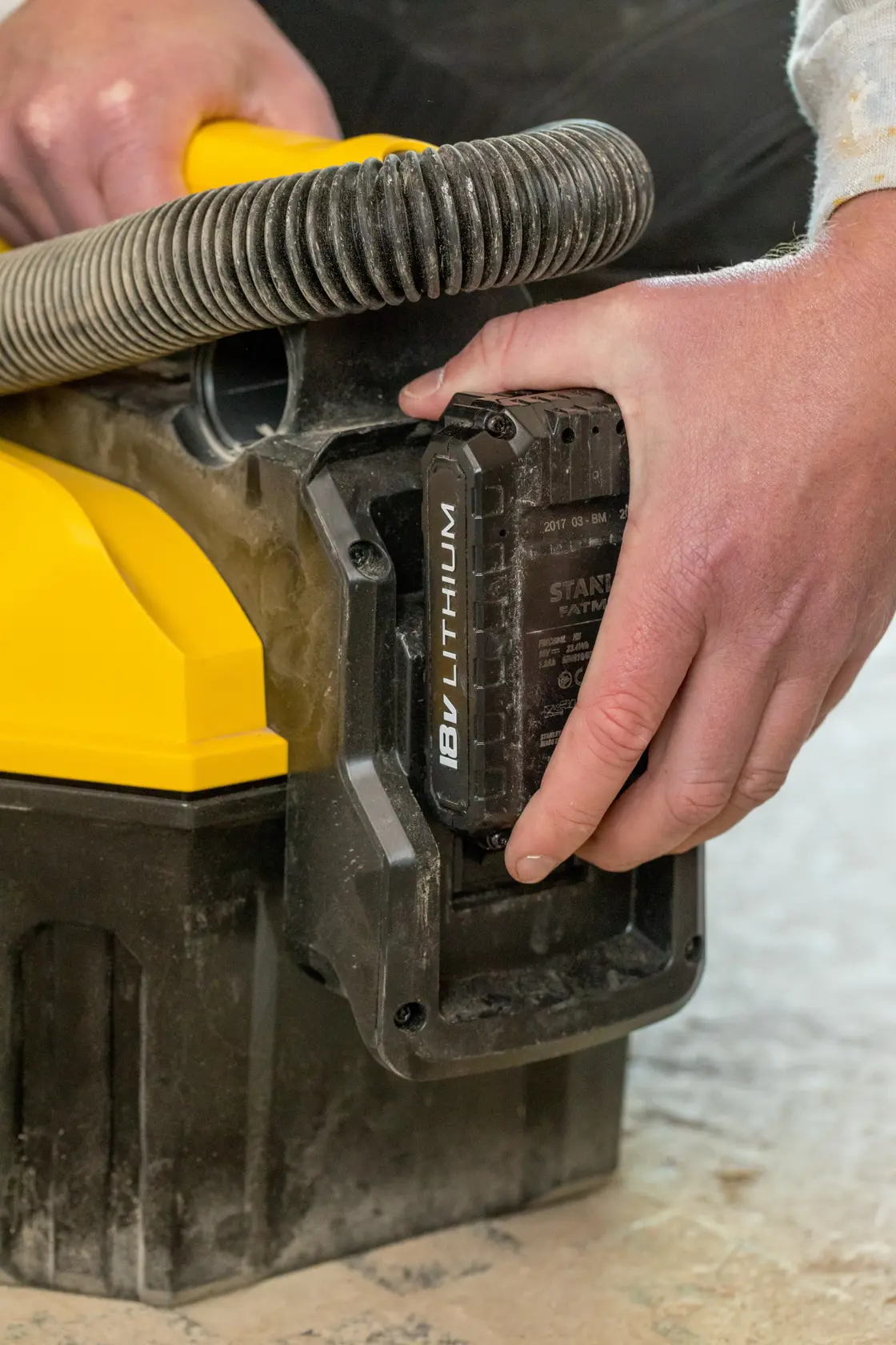 Foto vom STANLEY FMC795B Staubsauger mit Hand, die 18V Lithium-Akku einsetzt, Nahaufnahme des Akku-Fachs.