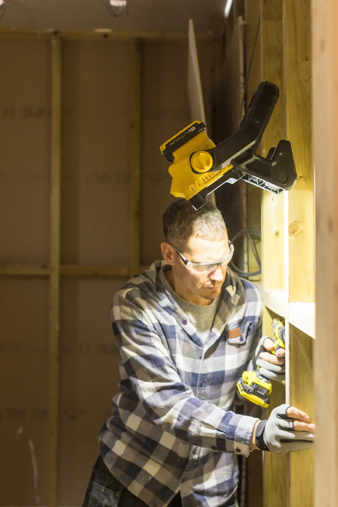 STANLEY FMCL001B Arbeitsleuchte an Holzträger befestigt, beleuchtet Arbeiter mit Bohrmaschine.