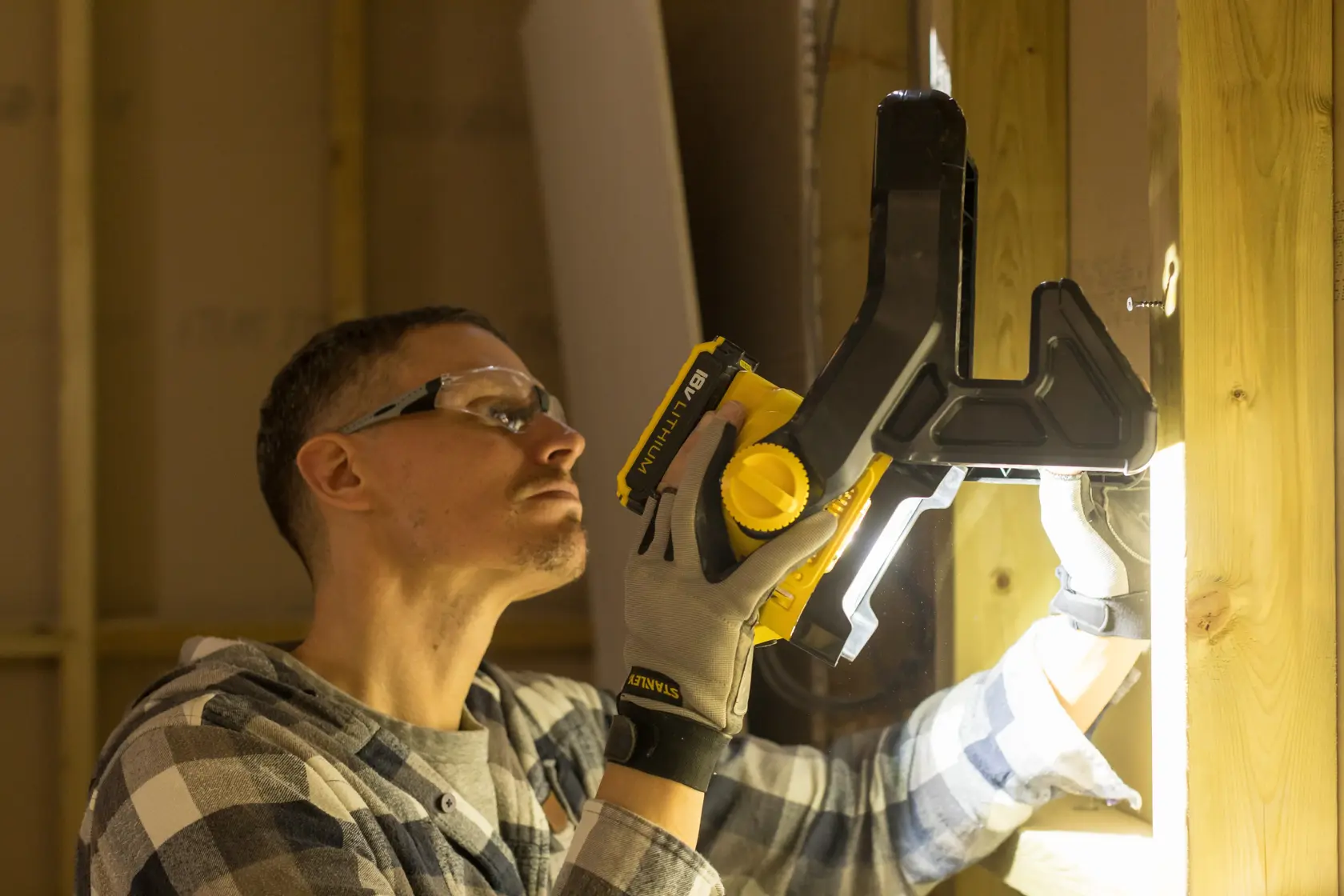 Foto der STANLEY FMCL001B Klemmleuchte im Einsatz an einem Holzträger, Arbeiter mit Handschuhen.
