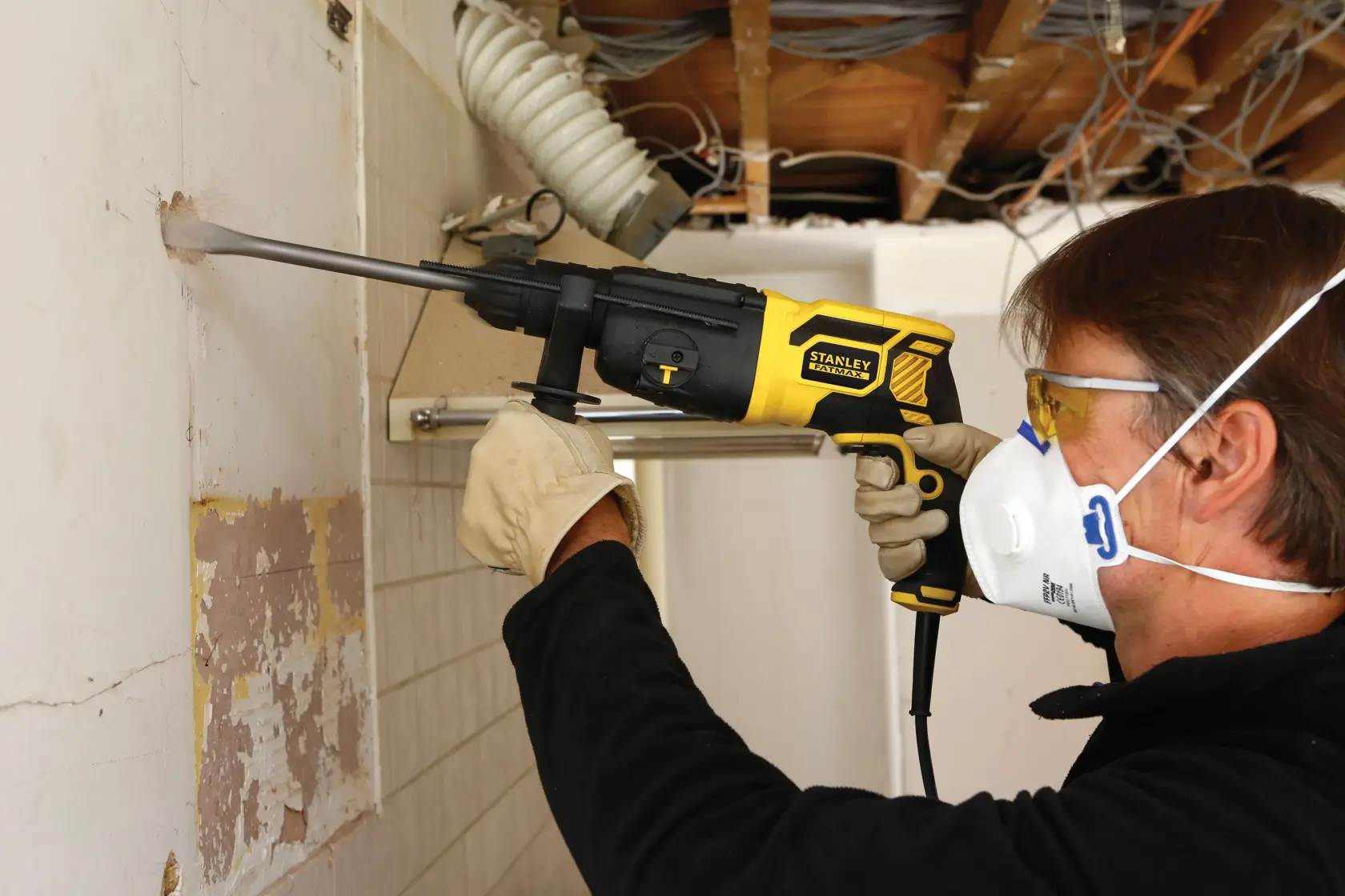 STANLEY FME500K rotary hammer used for wall demolition, side view, operator wearing gloves and mask.