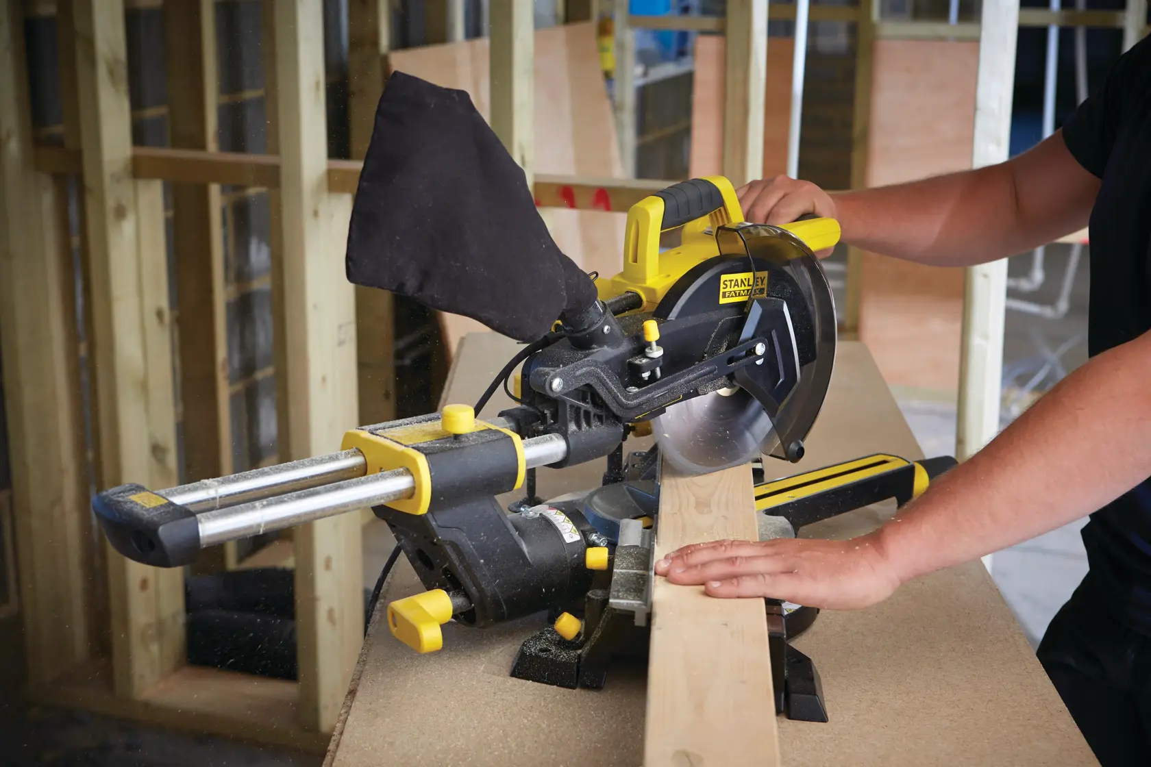 STANLEY FME721-QS miter saw in use, cutting a wooden board on a workbench at a construction site.