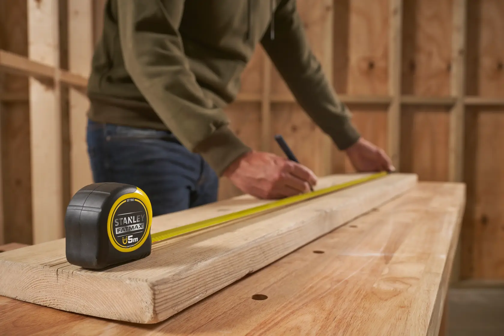 STANLEY FMHT0-33864 tape measure on wood in workshop setting, person marking measurement.