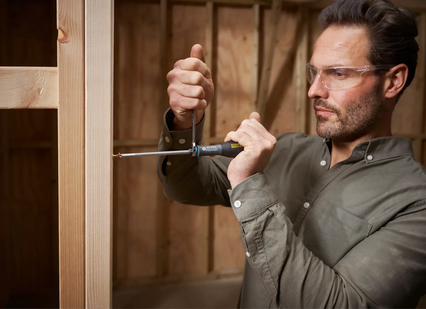 STANLEY FMHT0-62624 screwdriver in use by person attaching screw to wooden frame, close-up action shot.