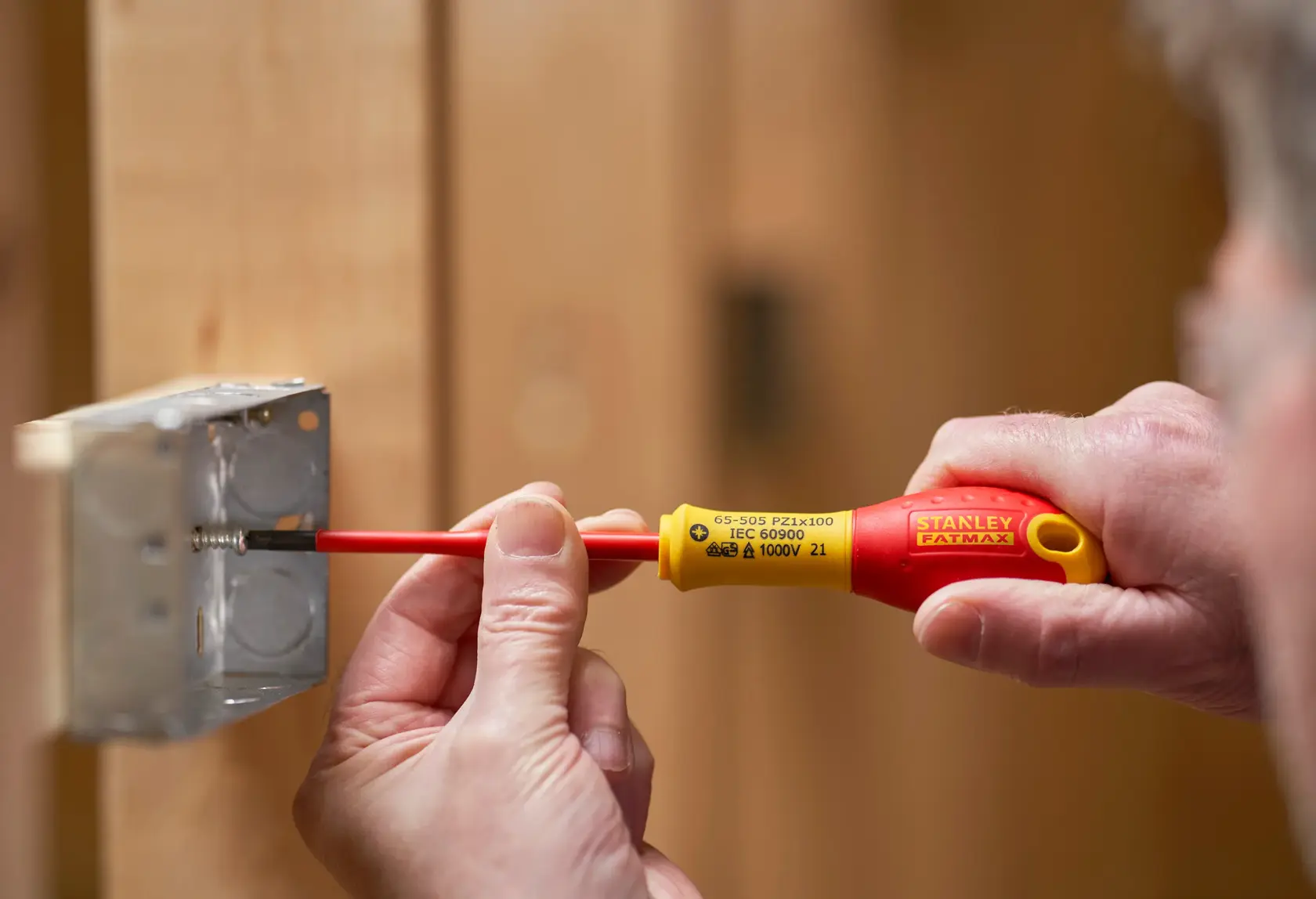 Stanley FMHT0-62649 insulated screwdriver used to tighten screw in metal electrical box, close-up view.
