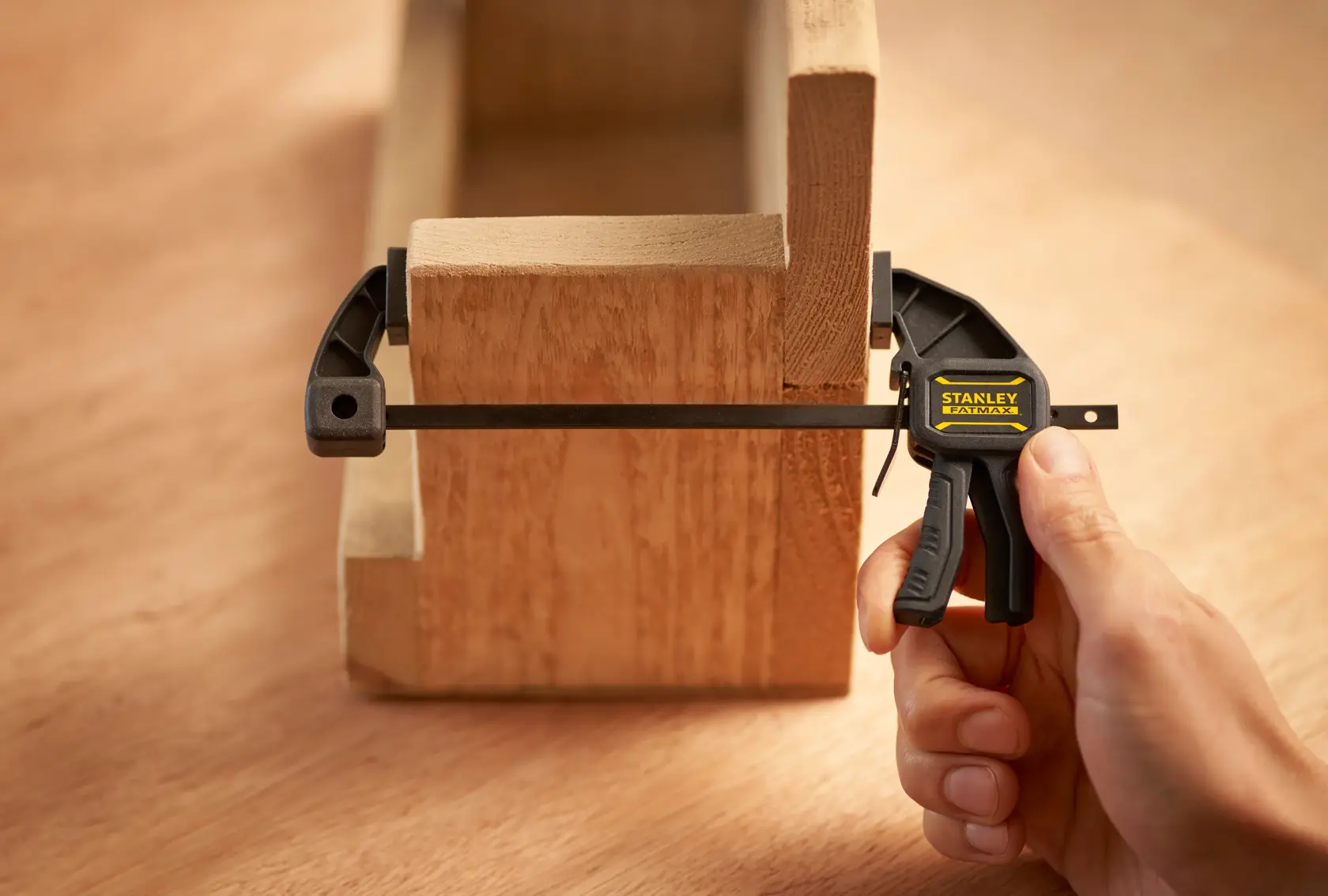 Photo of STANLEY FMHT0-83231 quick clamp holding two wooden pieces, close-up with hand operating clamp.