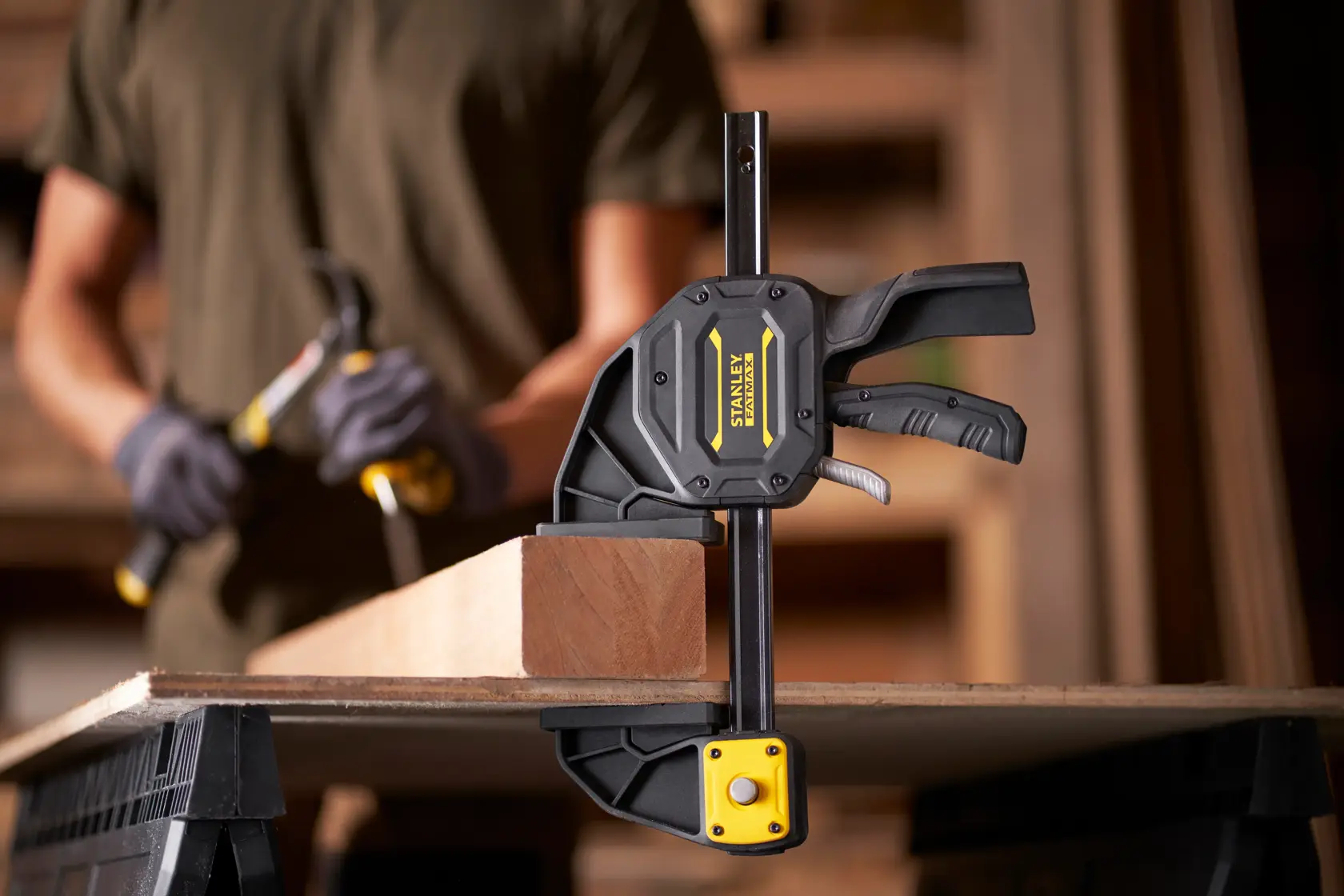 Stanley FMHT0-83238 trigger clamp securing wood on workbench, side angle view.