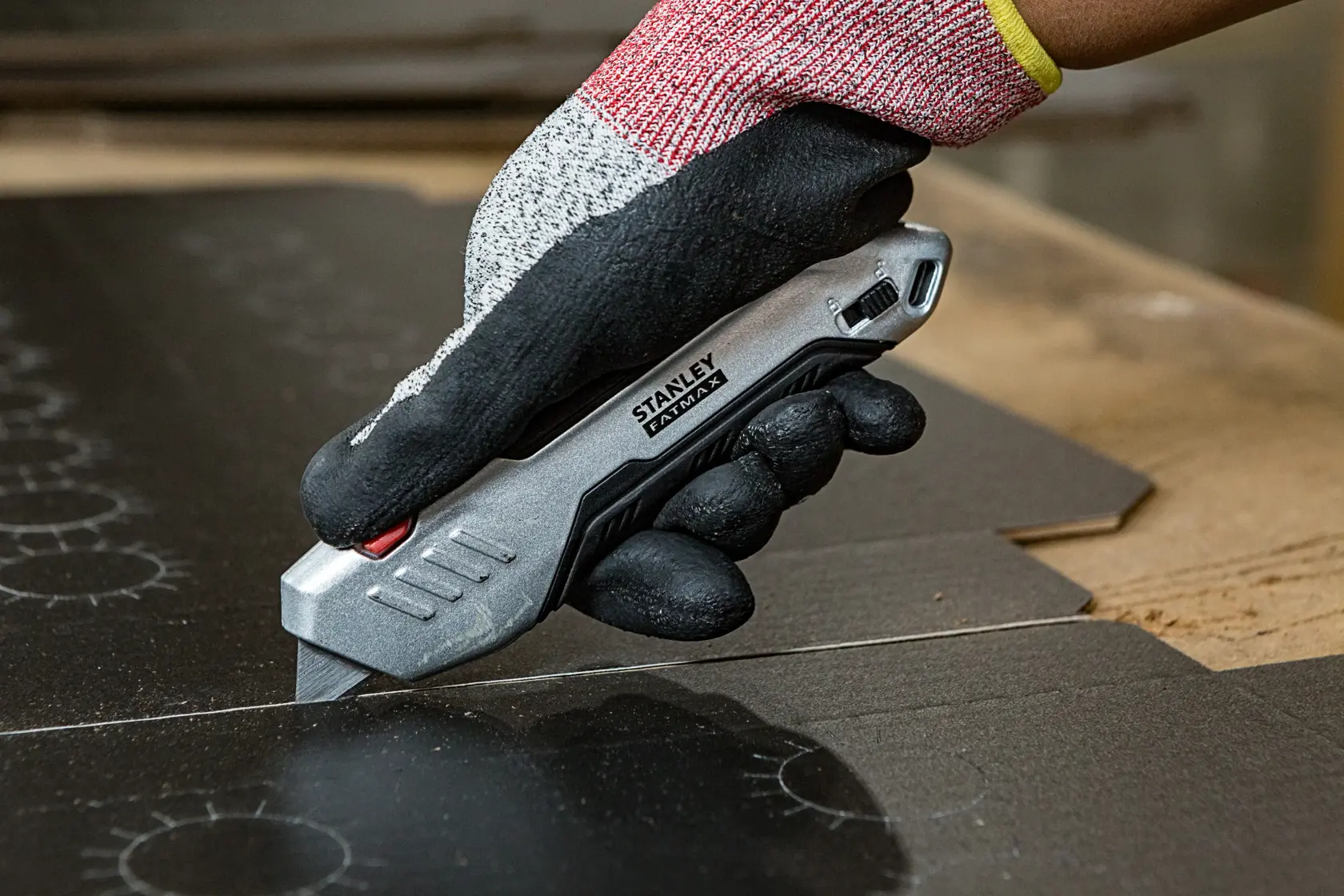 STANLEY FMHT10370-0 Universalmesser schneidet Karton, gehalten von einer behandschuhte Hand, Nahaufnahme.