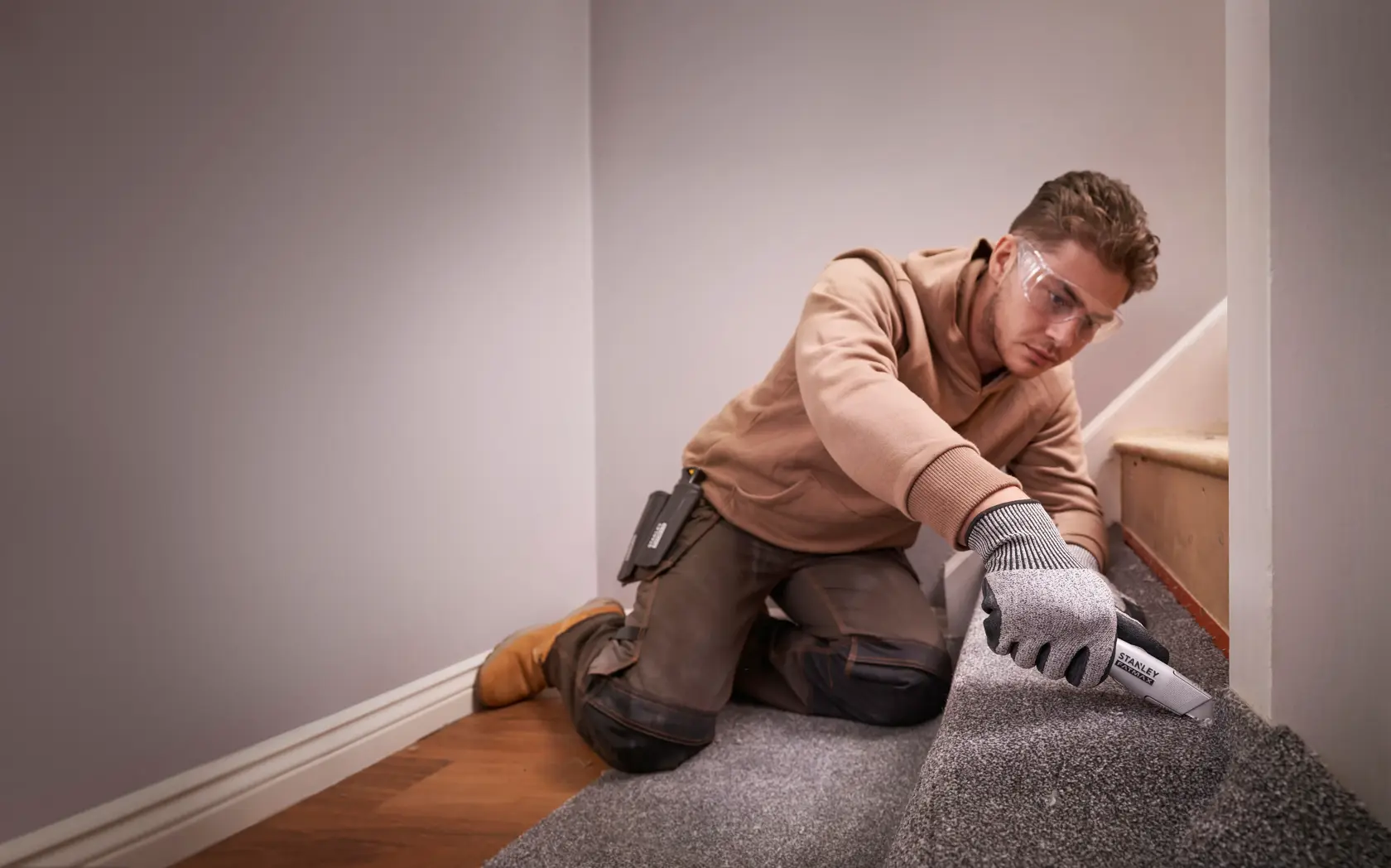 Foto eines Arbeiters, der mit dem STANLEY FMHT10501-0 Universalmesser Teppich auf einer Treppe schneidet.
