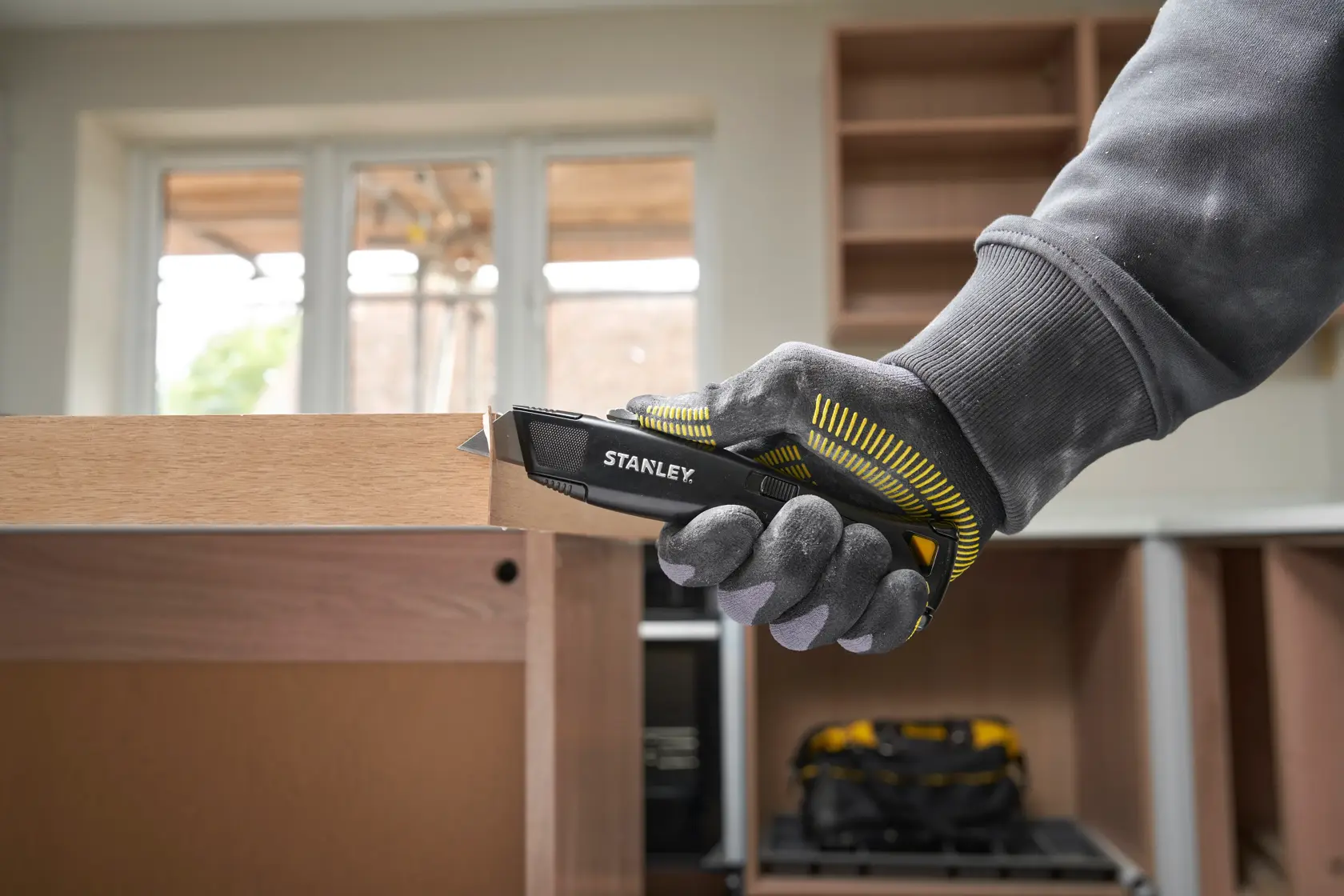 STANLEY FMHT10504-0 Universalmesser in behandschuhter Hand schneidet Holz, Innenbereich, Produkt Seitenansicht.