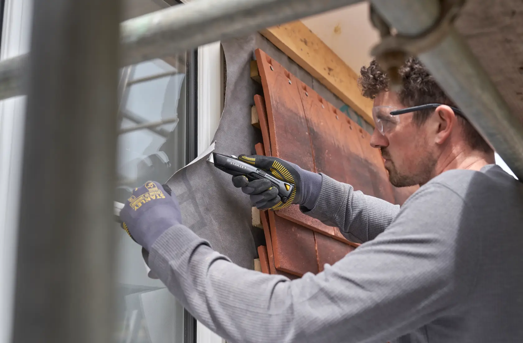 STANLEY FMHT10504-0 Universalmesser im Einsatz schneidet Baufolie an einem Fenster, Nahaufnahme bei Bauarbeiten.