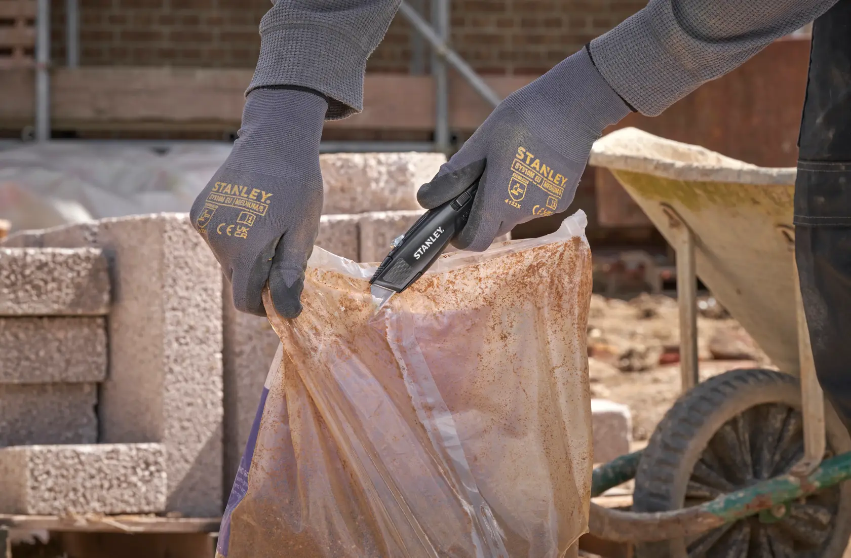 Foto eines Arbeiters, der das STANLEY FMHT10504-0 Universalmesser verwendet, um einen Plastiksack auf einer Baustelle zu öffnen.
